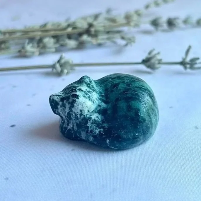 Natural Zoisite sleeping cat crystal carving with green and earthy tones on a neutral background.