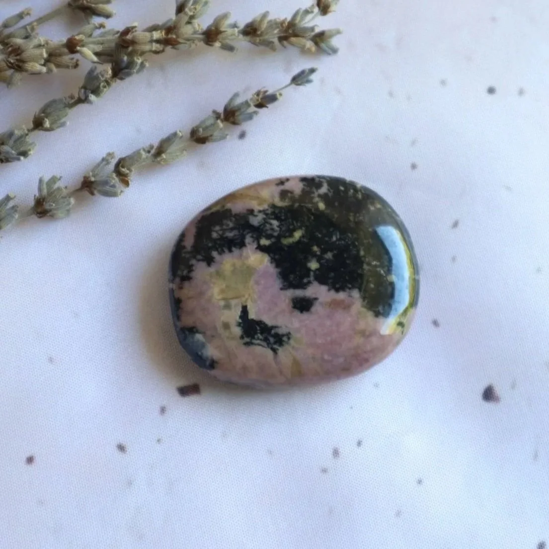 Natural Rhodonite flat stone held in hand for approximate size reference