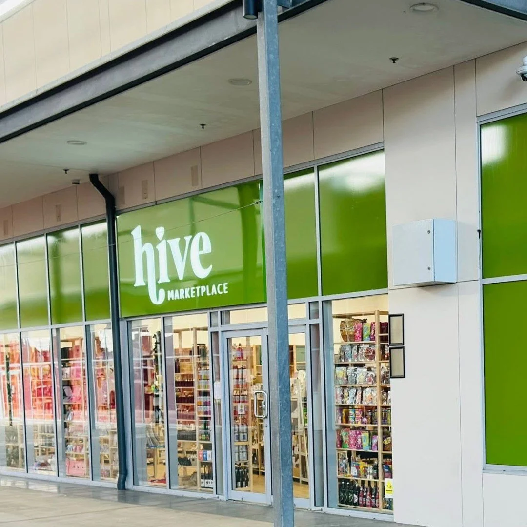 Exterior view of a Hive Marketplace store with a large green sign above the entrance and glass doors and windows showcasing products inside.