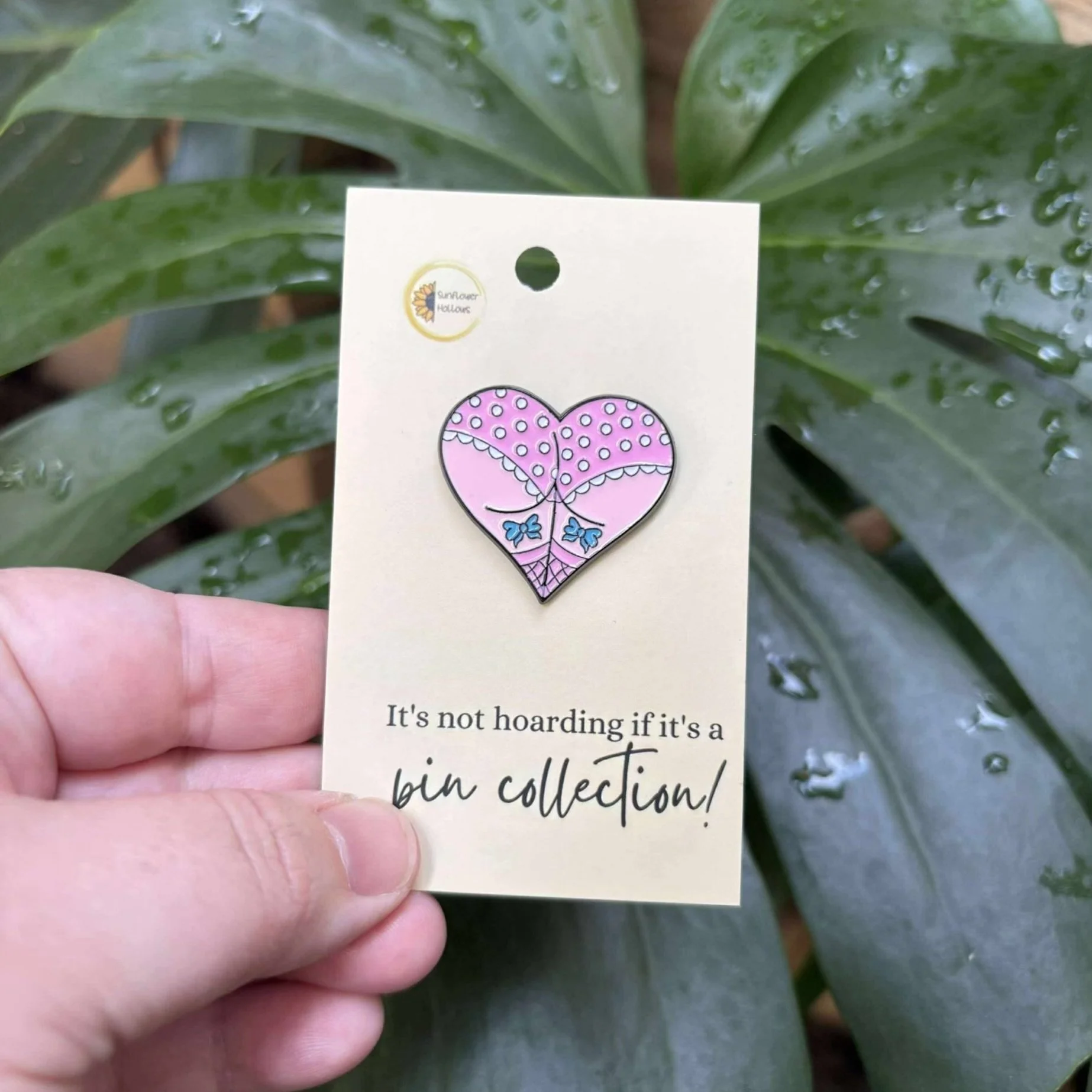 Enamel pin of a love heart featuring a cheeky butt wearing pink undies with blue bows, quirky and playful accessory
