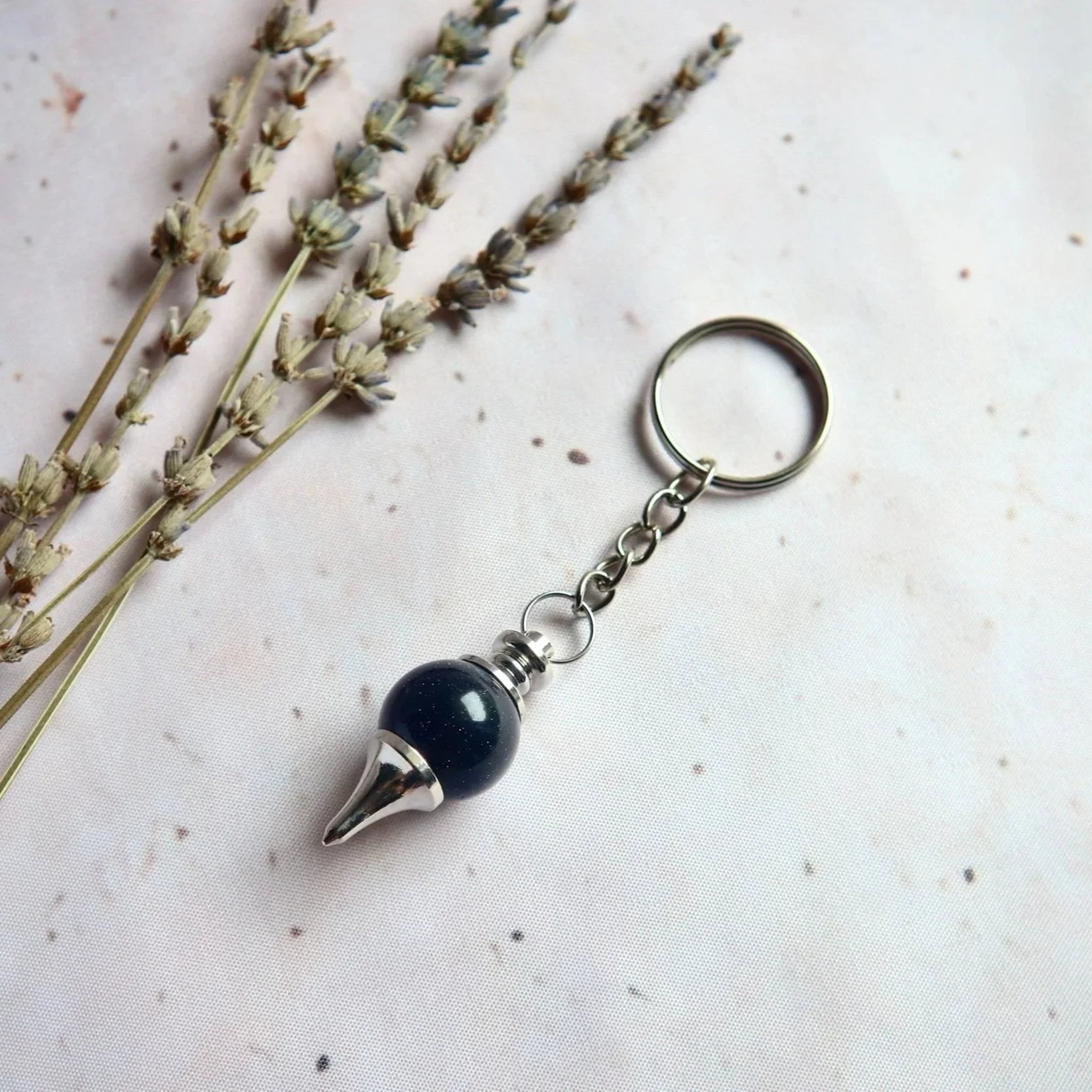 Pendulum-style keyring featuring a rounded decorative bead and silver-tone pointed fitting.