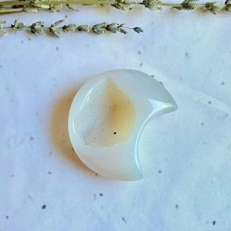 Pale grey and lavender-purple Agate crescent moon crystal carving held in a hand