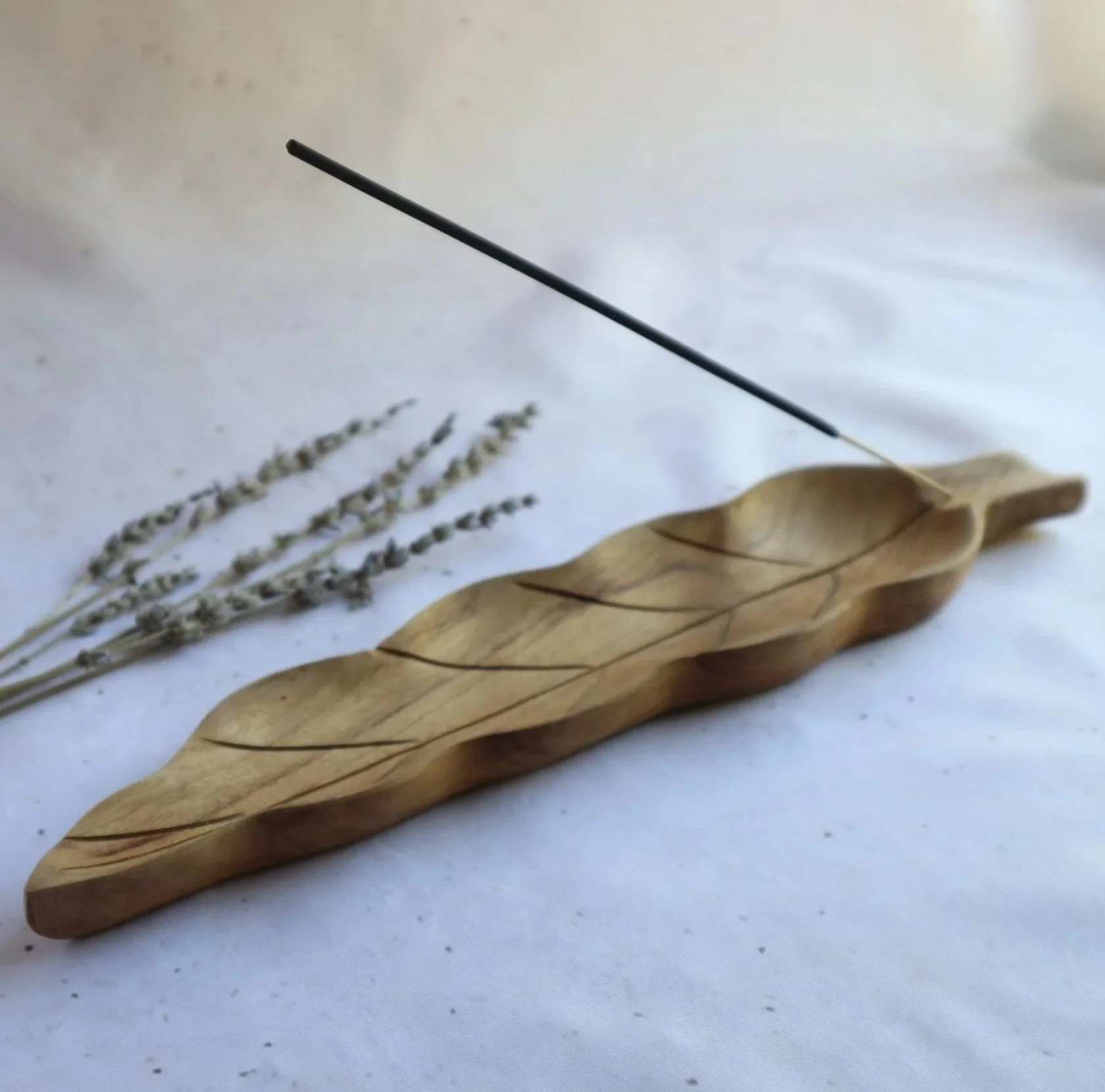 Handcrafted wooden leaf incense holder displayed on a soft cream background with dried lavender.