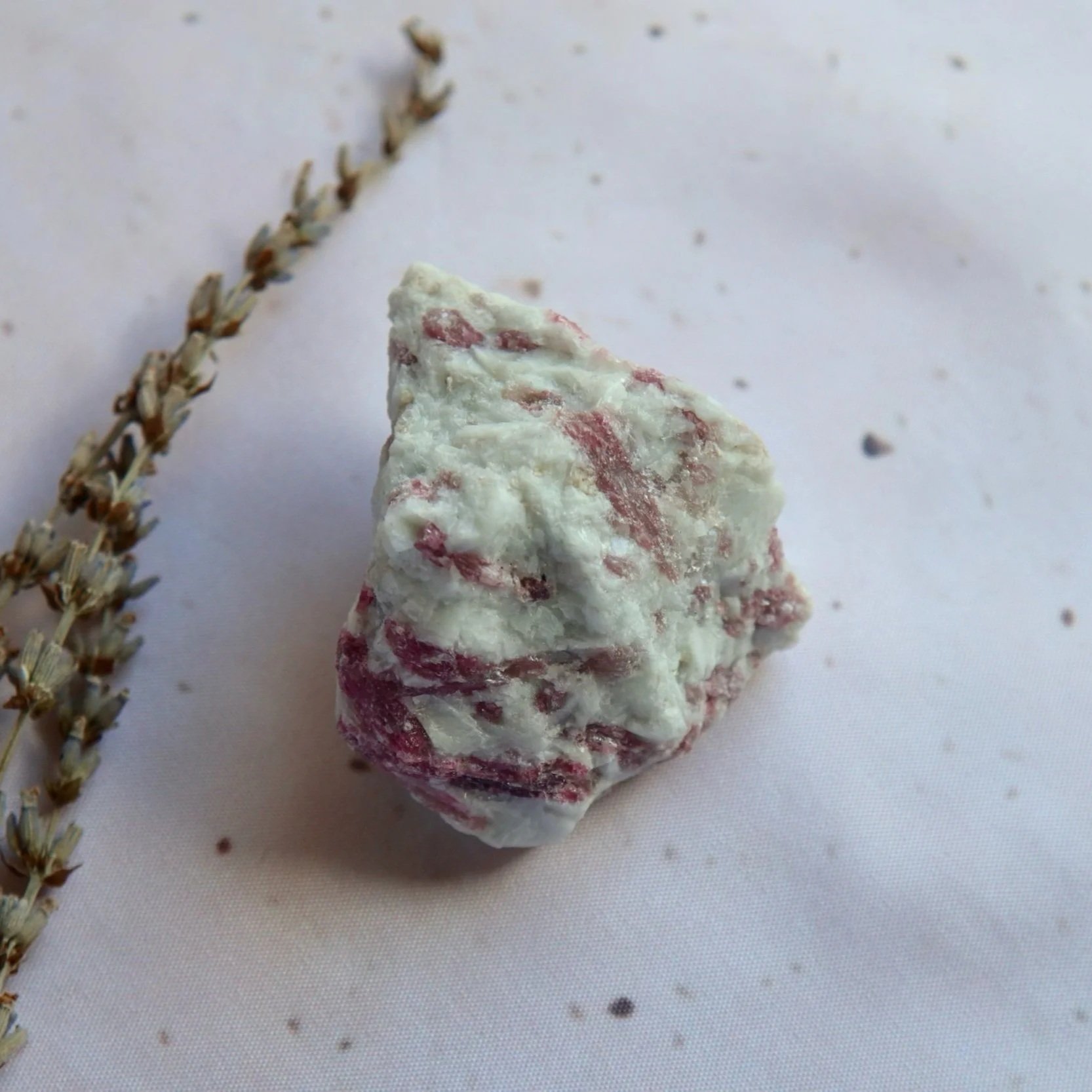 Exact rough mineral specimen photographed from above, showing its pink-red markings, white areas and rugged surface.