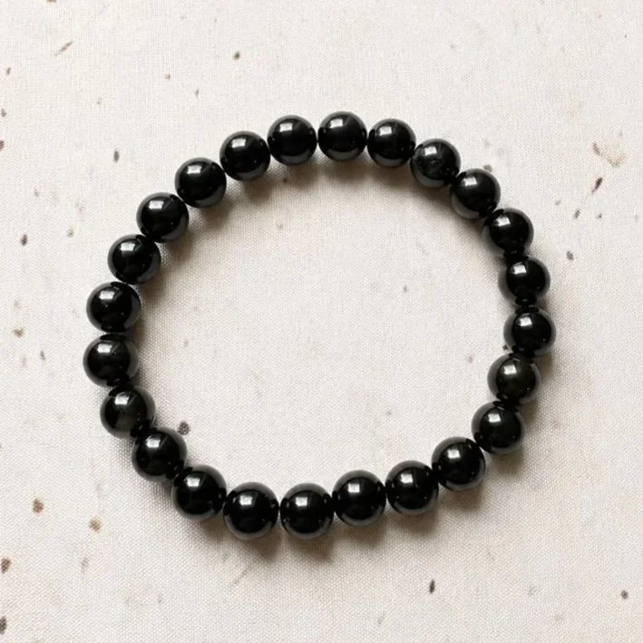 Black Obsidian crystal bracelet with smooth round beads on stretch elastic, displayed on a neutral background.