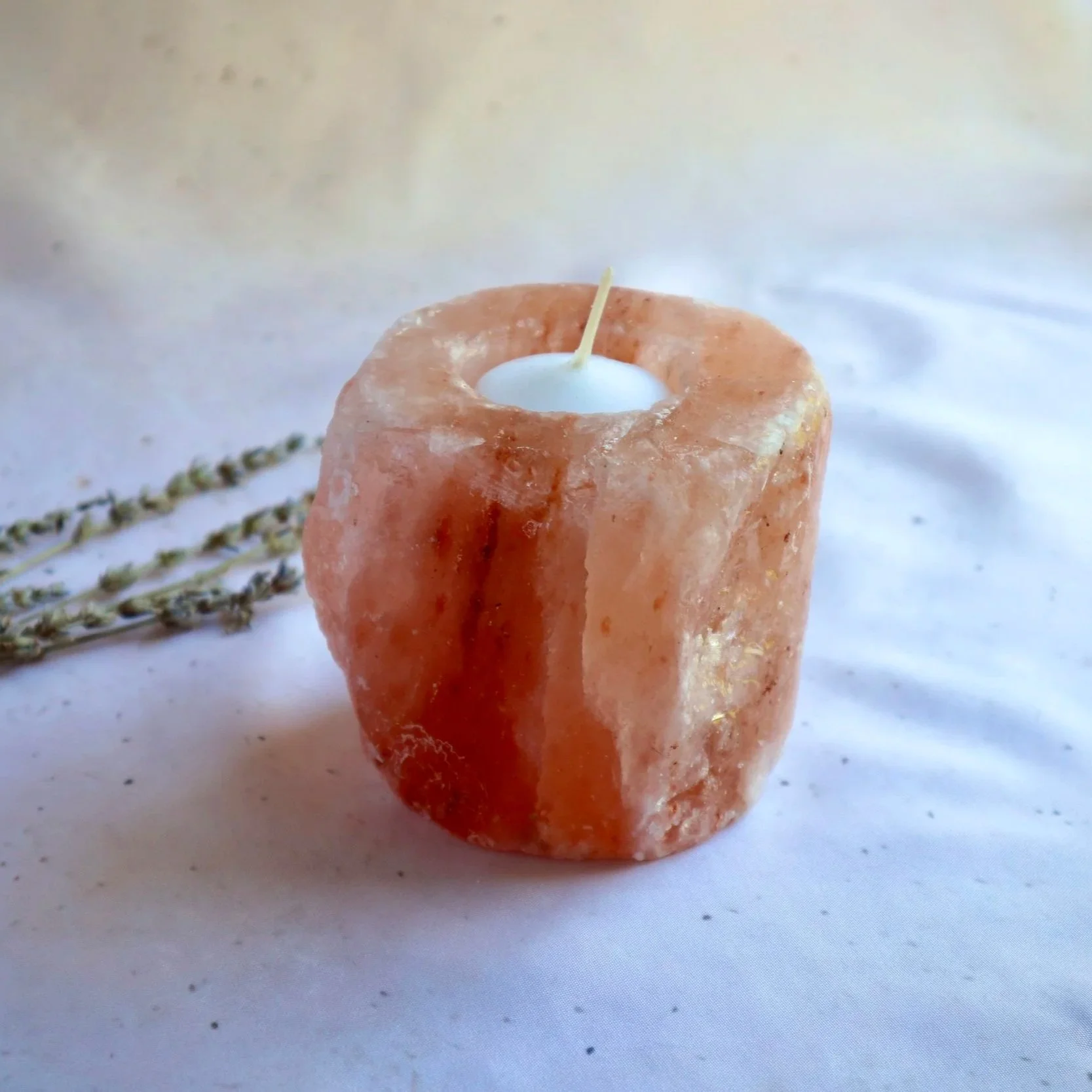 Natural Himalayan Salt candle holder with warm pink crystal tones on a cream fabric background.
