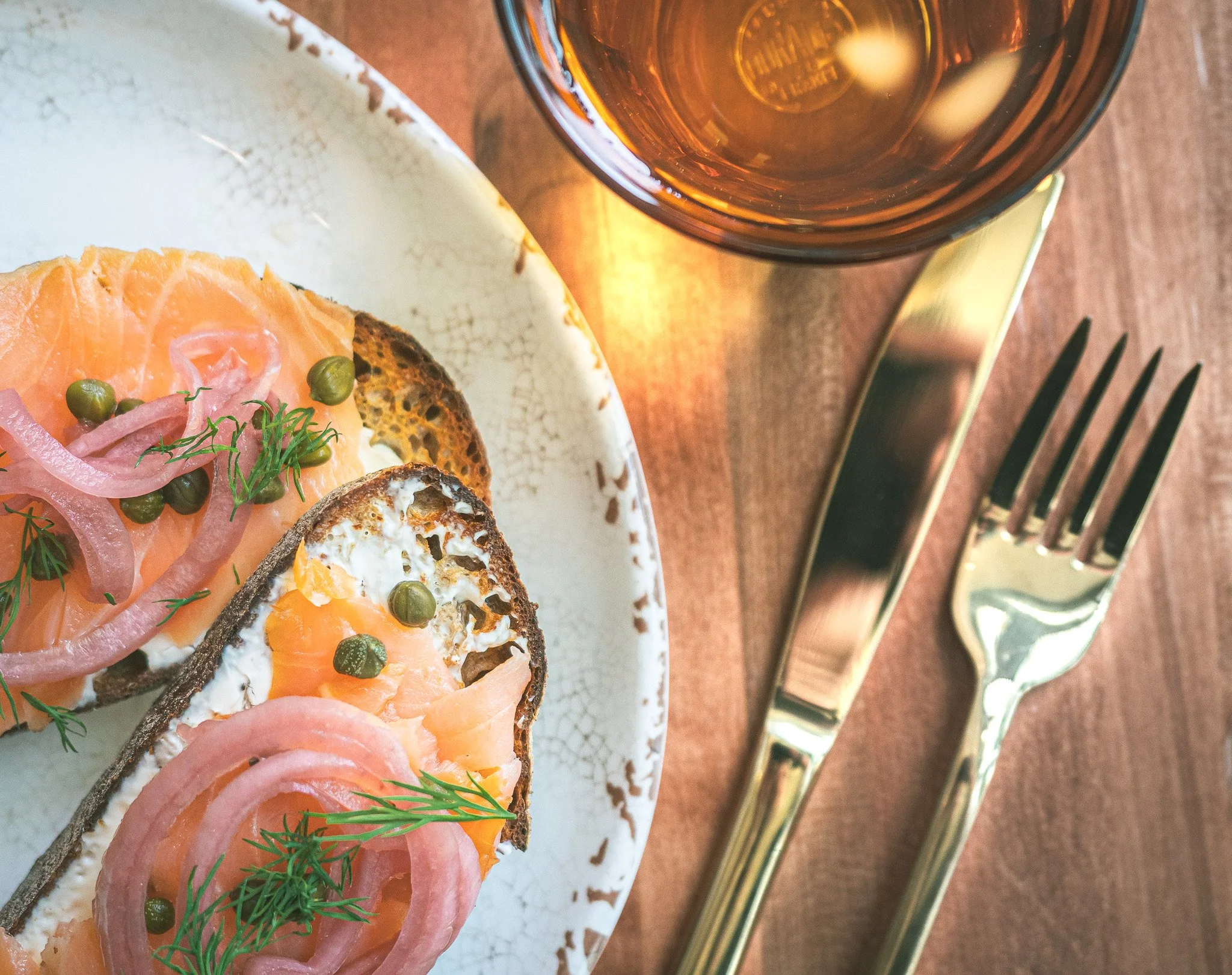 top down view of lox toast on night move sourdough bread with gold cutlery and glass of water