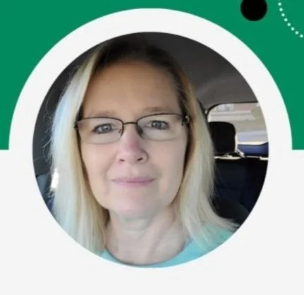 A woman with blonde hair and glasses sitting in a car, looking at the camera.