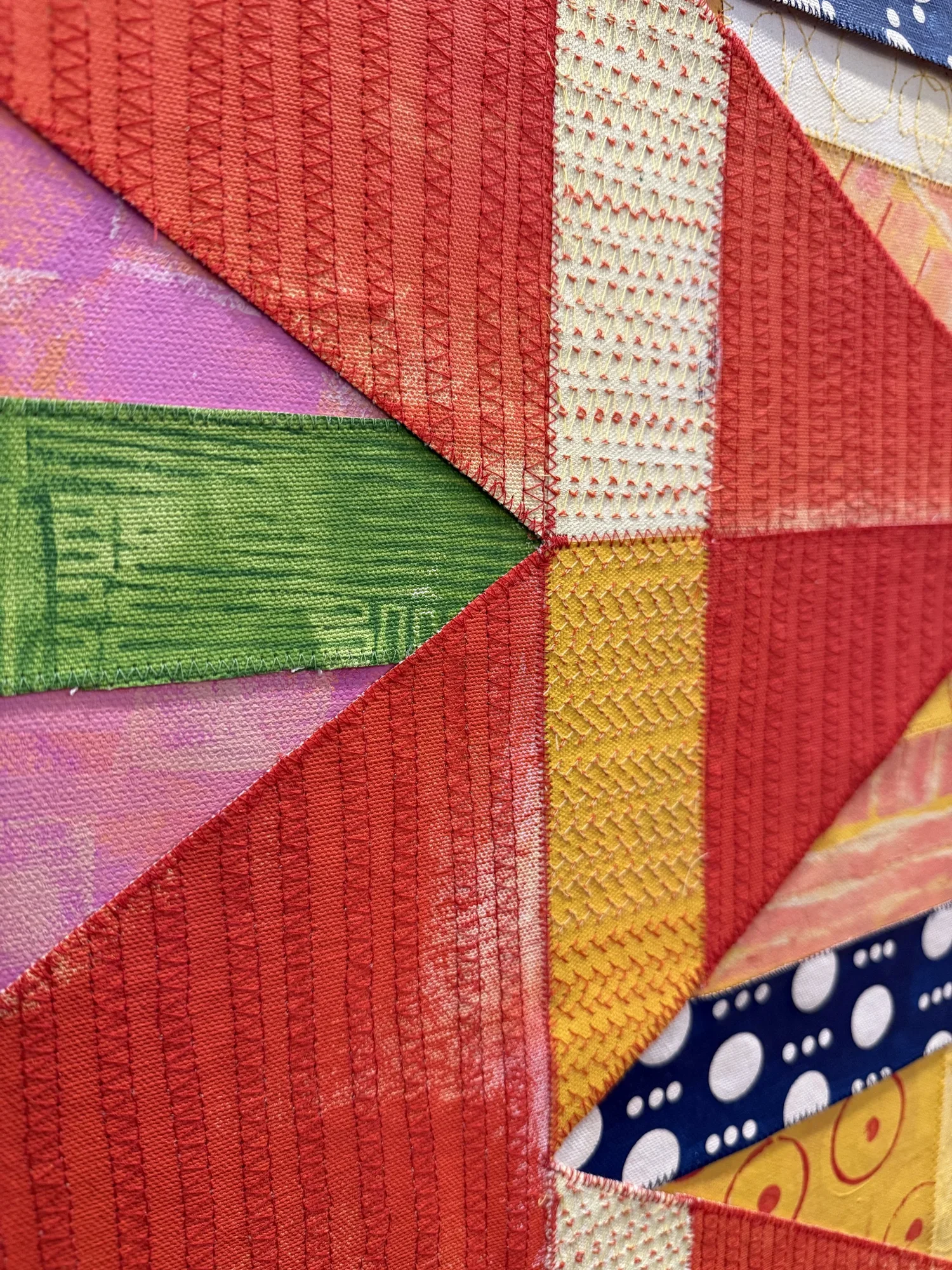 Close-up of colorful fabric patchwork with various stitchings and textures, including red, yellow, pink, and blue fabrics.