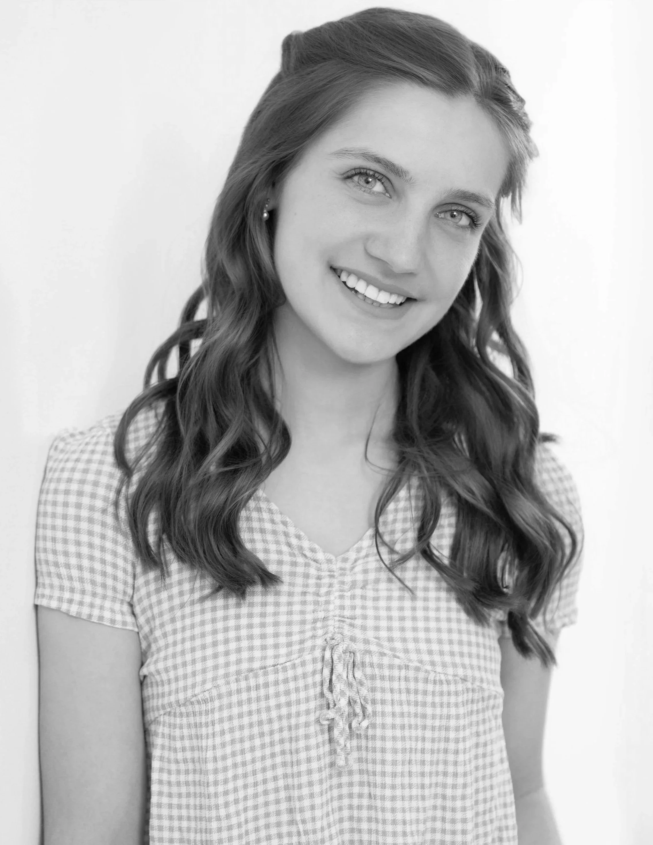 Black and white photo of a smiling woman with wavy hair wearing a checkered dress.