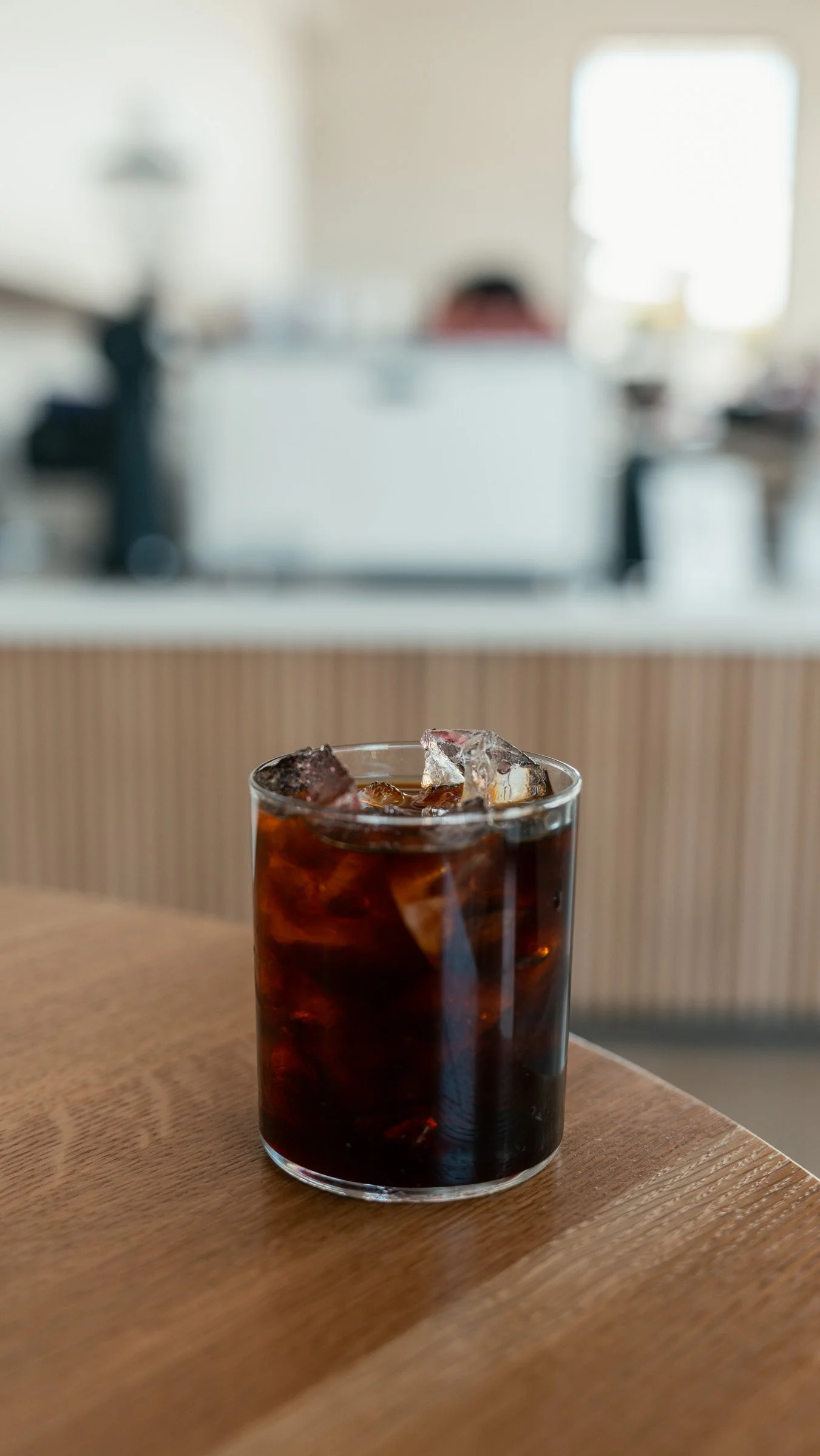 A glass of iced cola with ice cubes on a wooden table in a cafe.