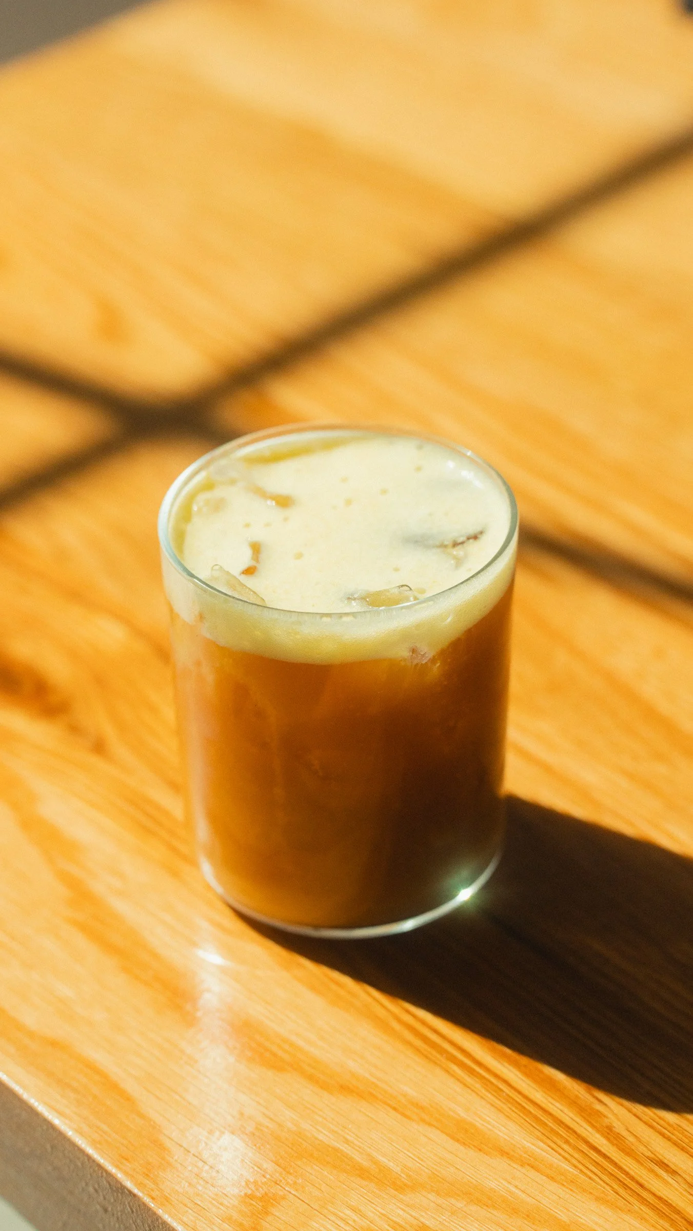 A glass of beer on a wooden surface with sunlight creating a shadow.