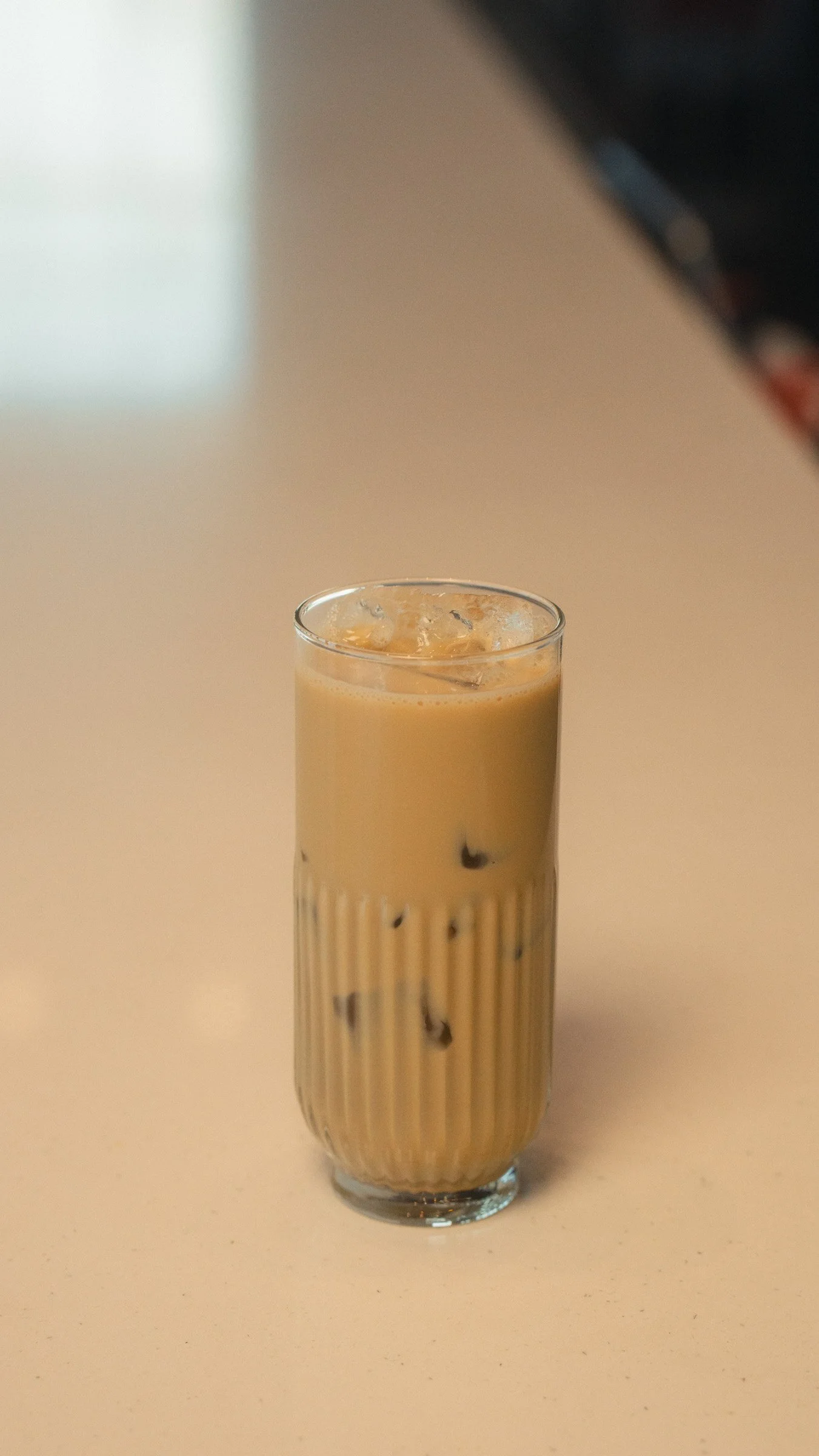 A tall glass of iced coffee with milk on a beige surface.