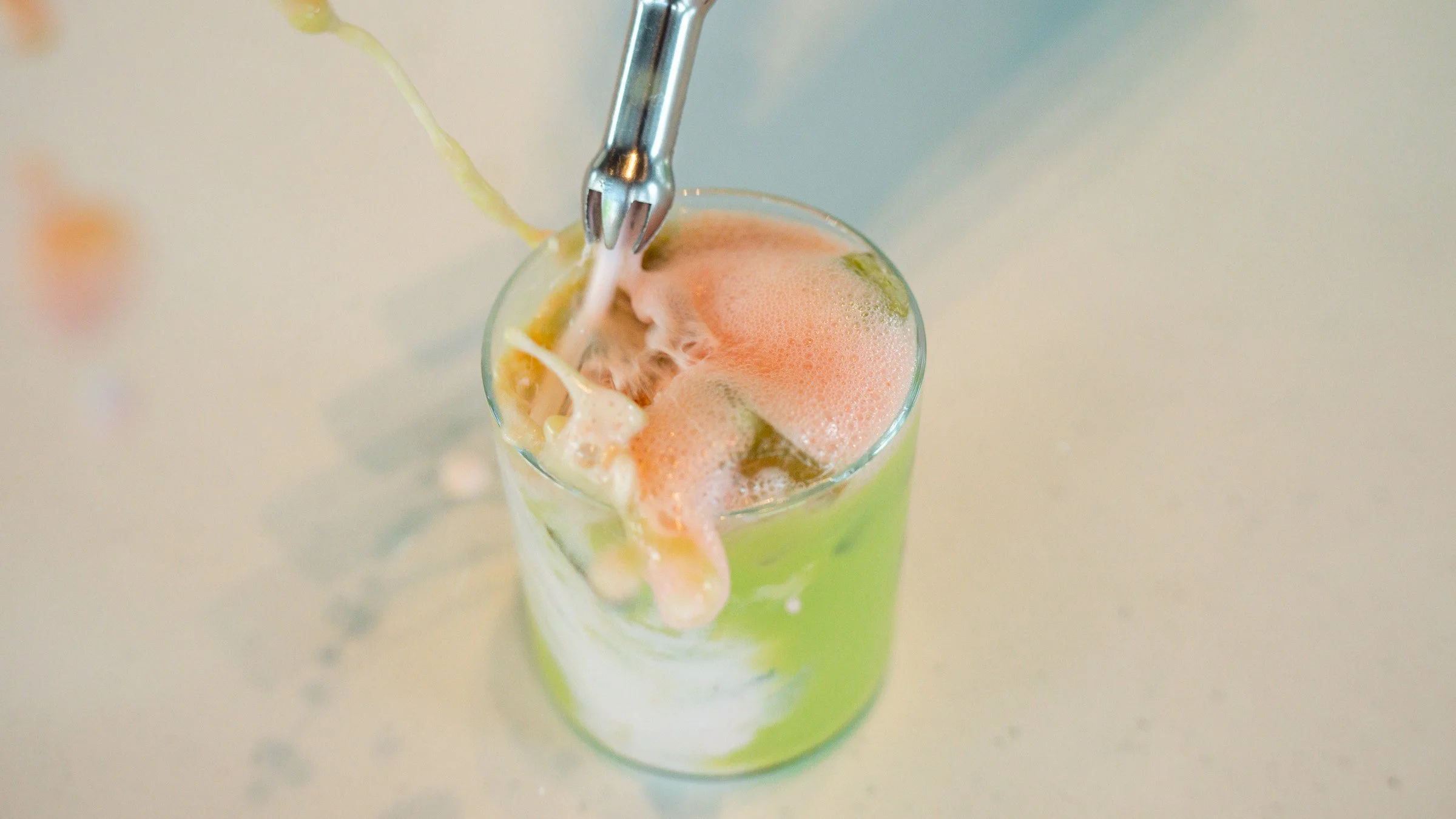 A glass of a beverage with foam and a straw, with some foam and ingredients overflowing from the top.