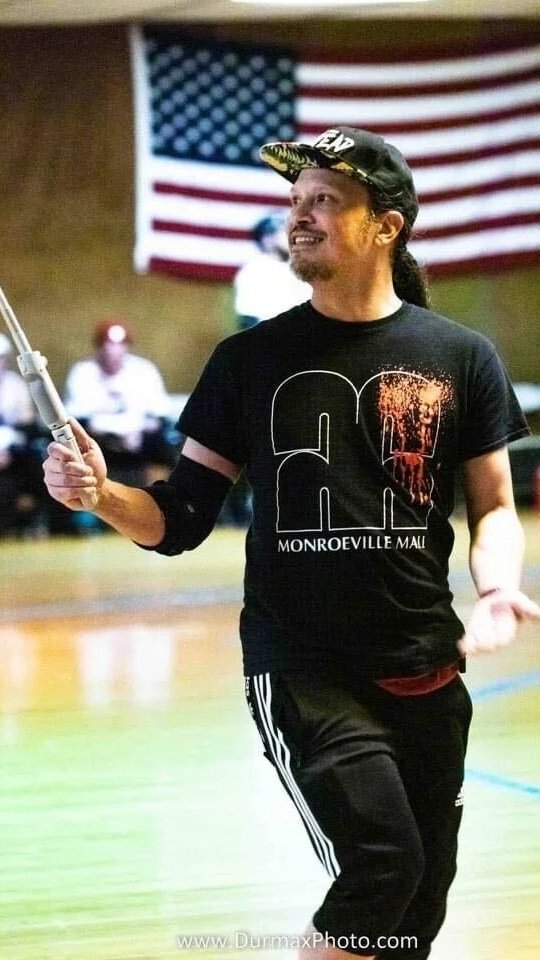 Man smiling while holding a flag in an indoor gymnasium, with an American flag hanging in the background.