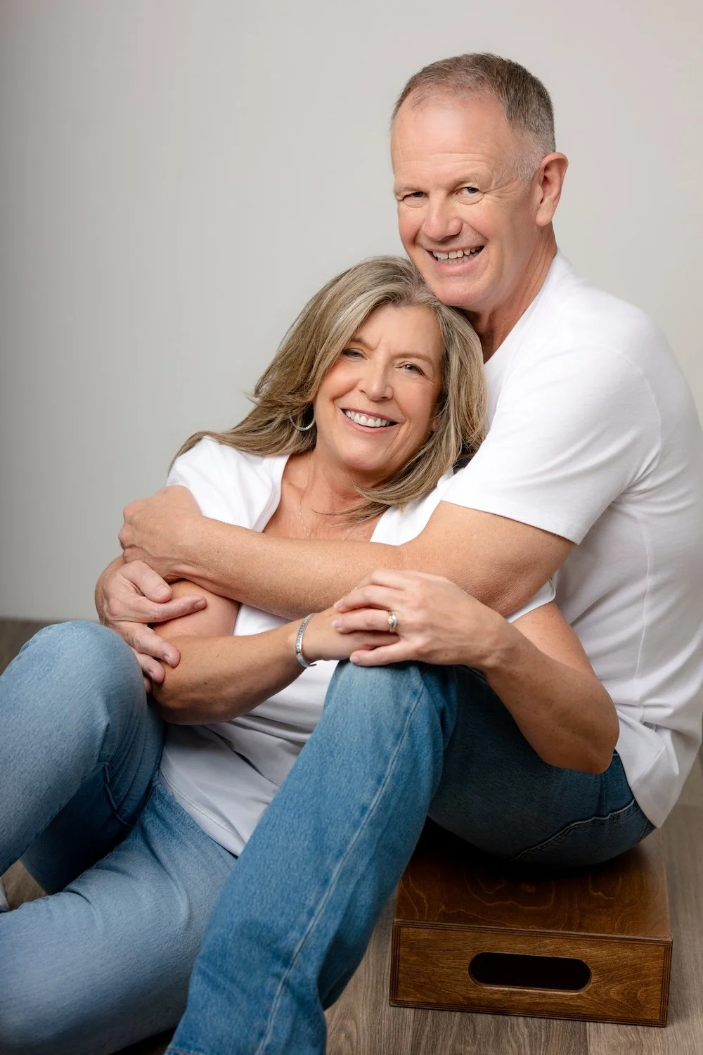 Smiling couple embracing in white shirts and blue jeans during a studio portrait session