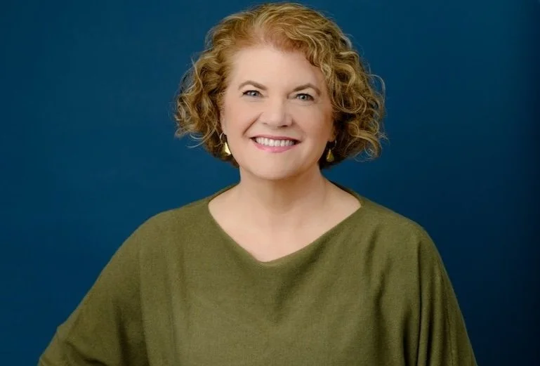 Professional headshot of a smiling woman on a blue background