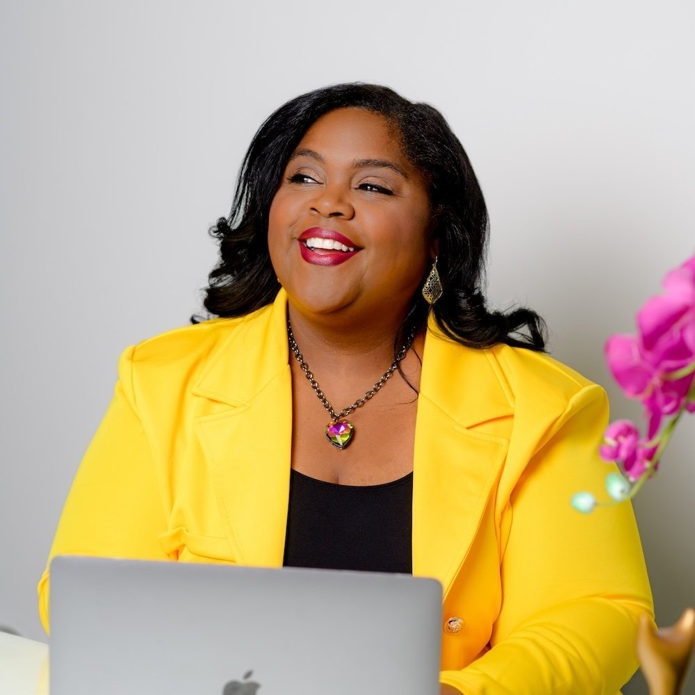 Headshot of Black woman in a yellow blazer smiling to the side