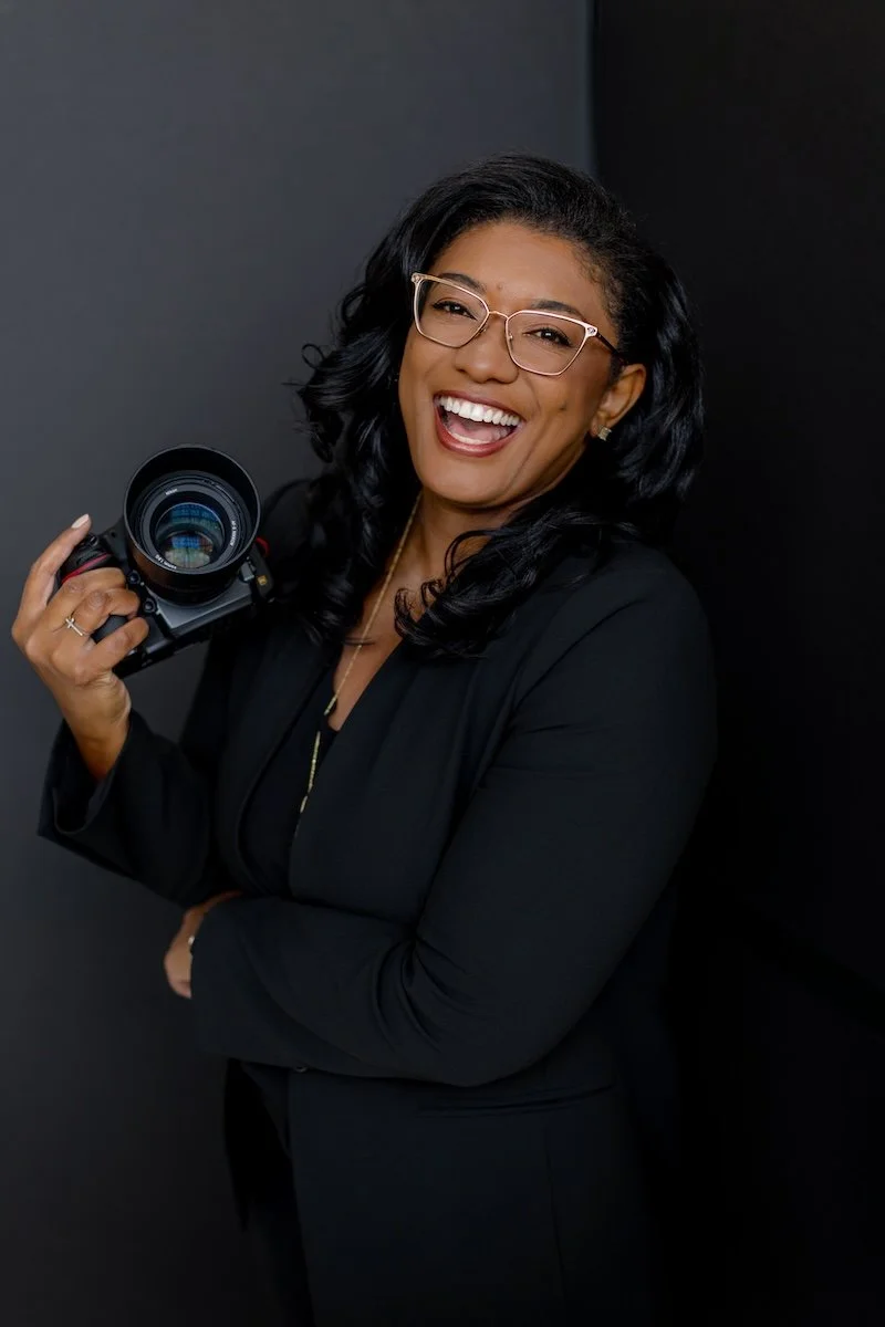 Shala Wilson smiling while holding a camera in her photography studio
