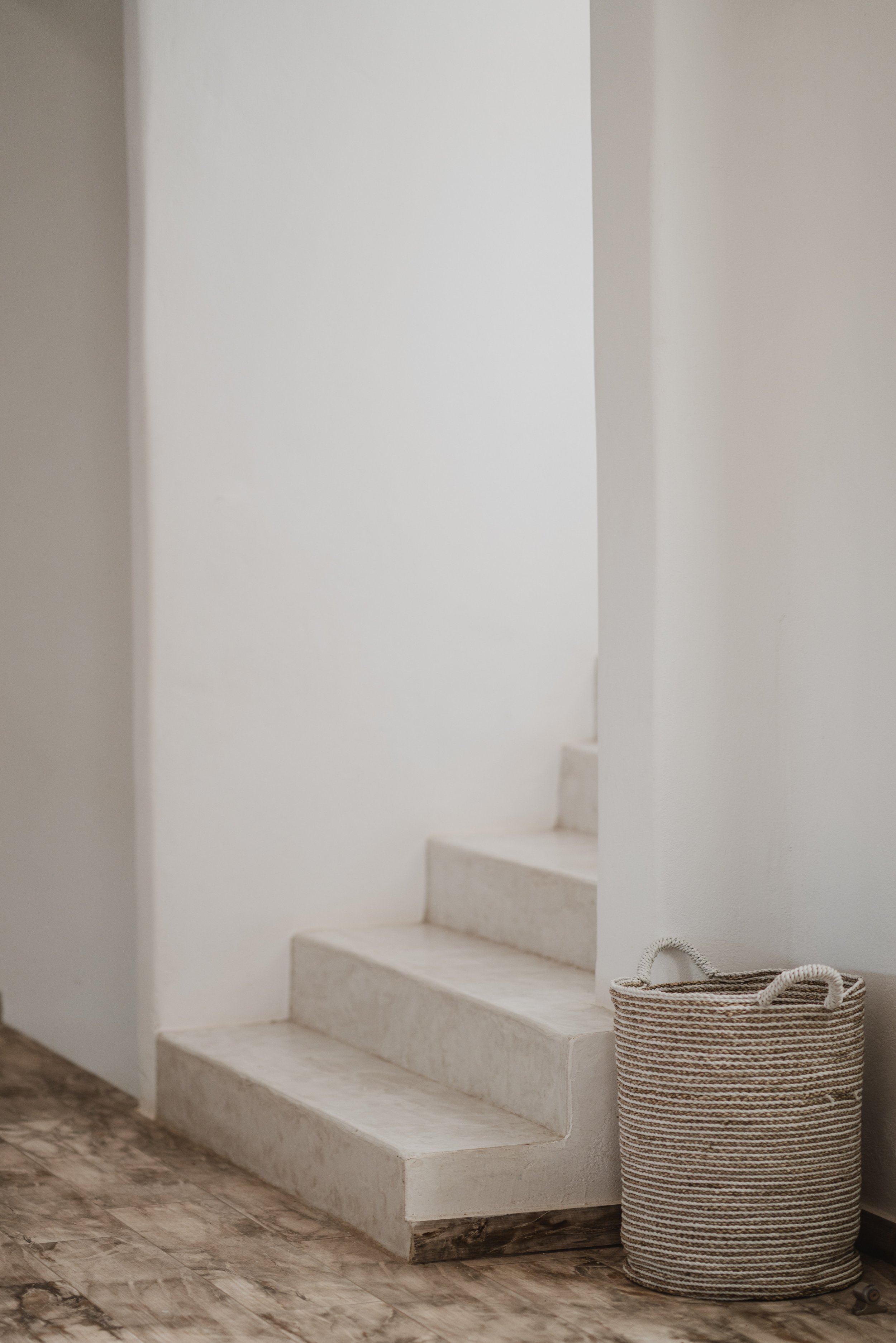 White stairs next to a textured basket on a wooden floor in a minimalist interior.