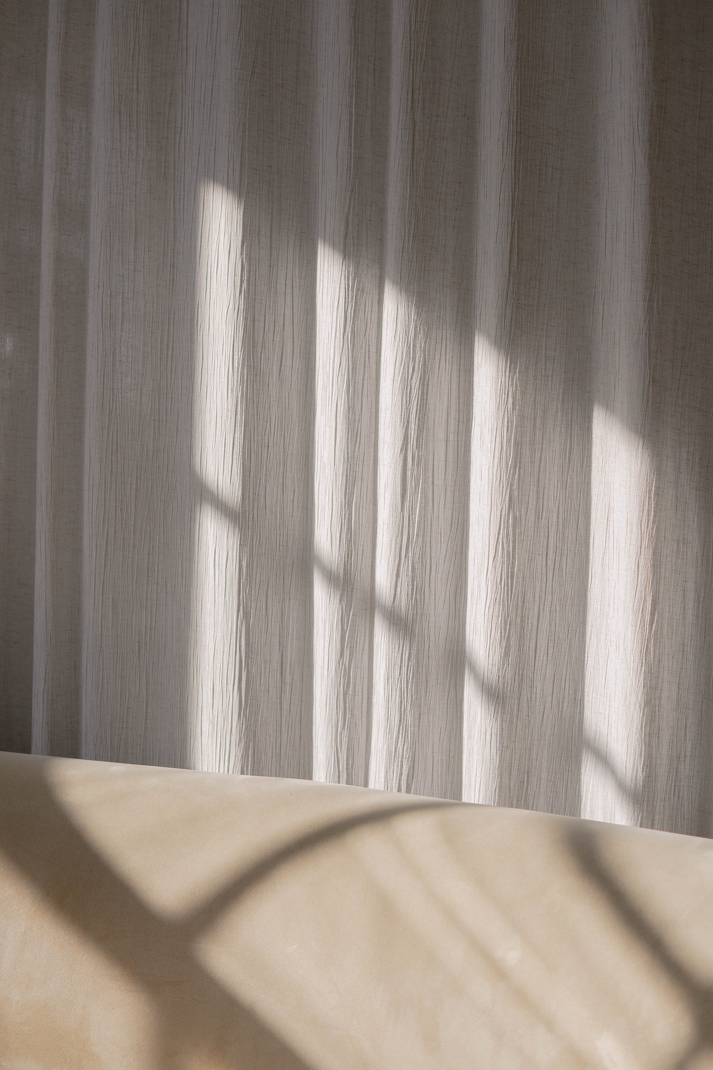 Sunlight filtering through curtain with window pattern shadows on beige surface.