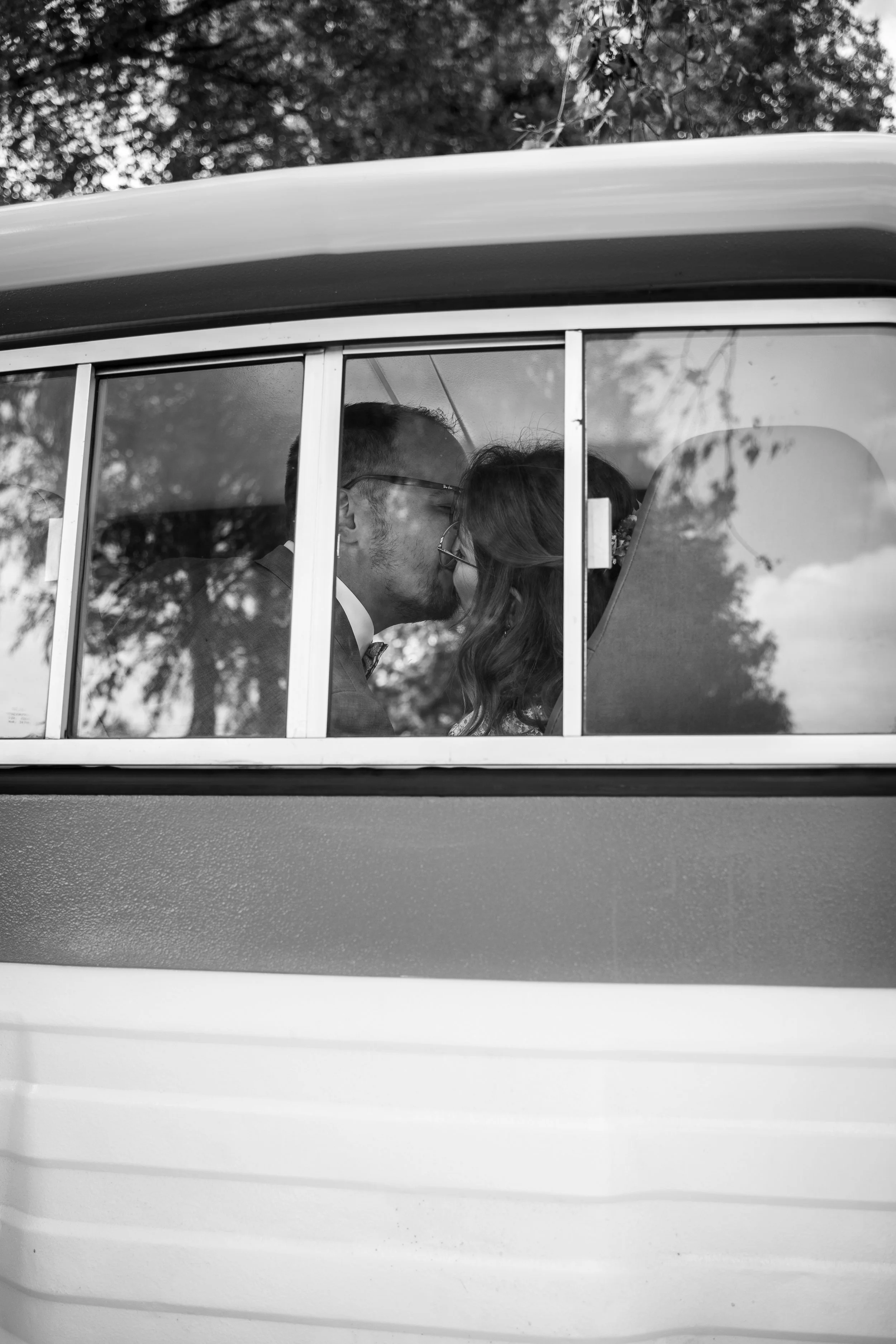 Ein schwarz-weiß Foto eines Autos von außen, durch das ein Paar beim Küssen im Inneren des Fahrzeugs zu sehen ist.