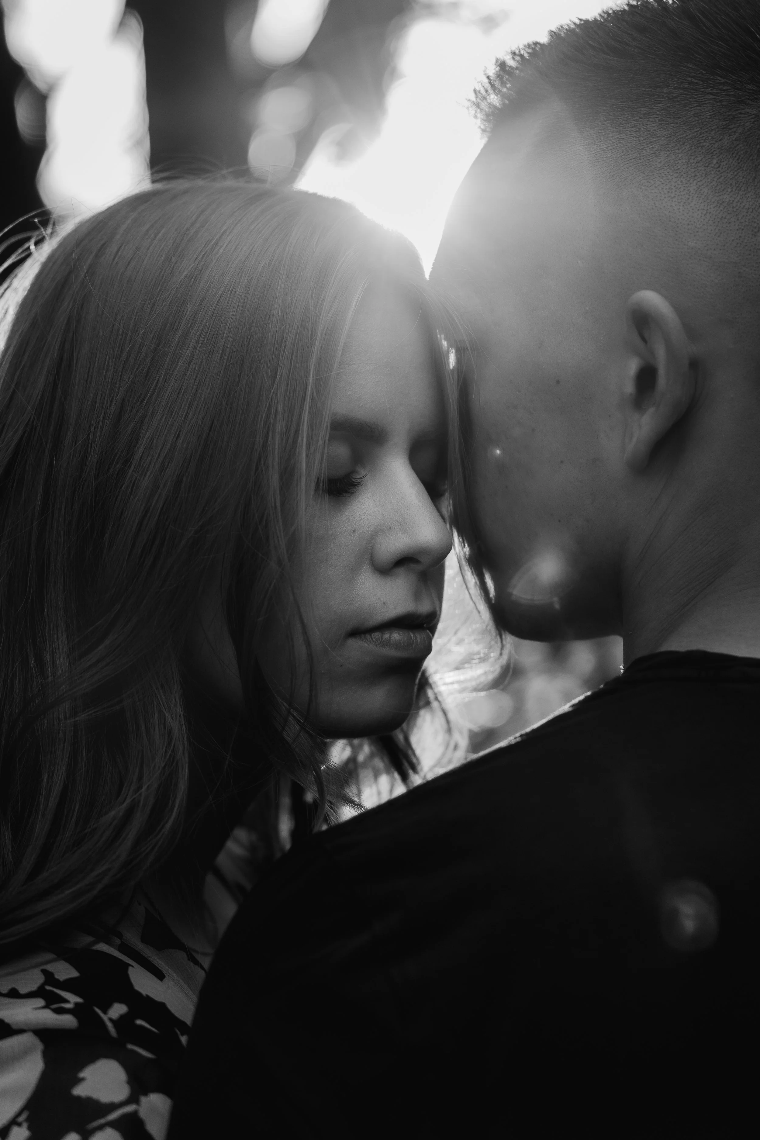 Ein Mann und eine Frau stehen sich sehr nah, fast küssend. Das Bild ist schwarz-weiß, die Frau hat lange, glatte Haare und trägt ein Kleid mit Muster, der Mann hat kurze Haare.