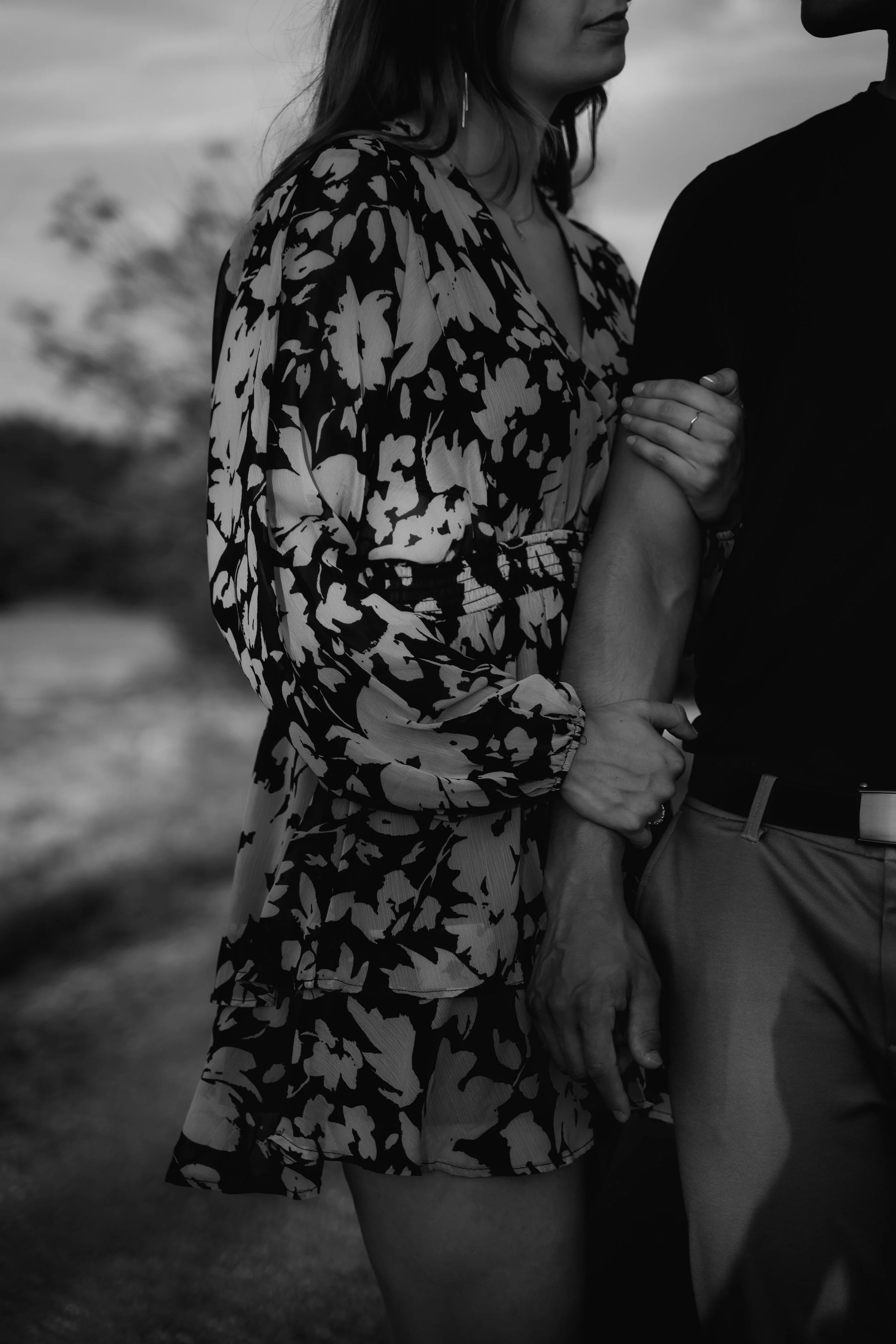 Zwei Menschen, eine Frau und ein Mann, die sich an den Händen halten. Die Frau trägt ein Kleid mit auffälligem schwarz-weißen Muster, während der Mann nur teilweise sichtbar ist.