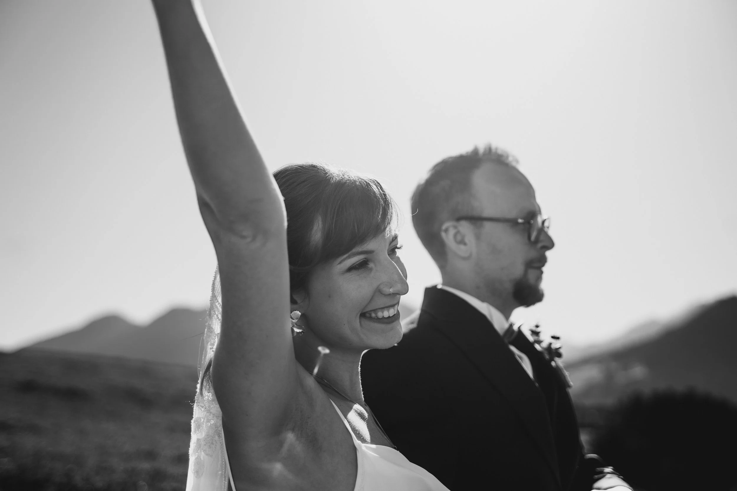 Ein glückliches Brautpaar bei der Hochzeit, die an einem sonnigen Tag draußen im Freien steht, mit lächelnden Gesichtern, während sie den Moment genießen.