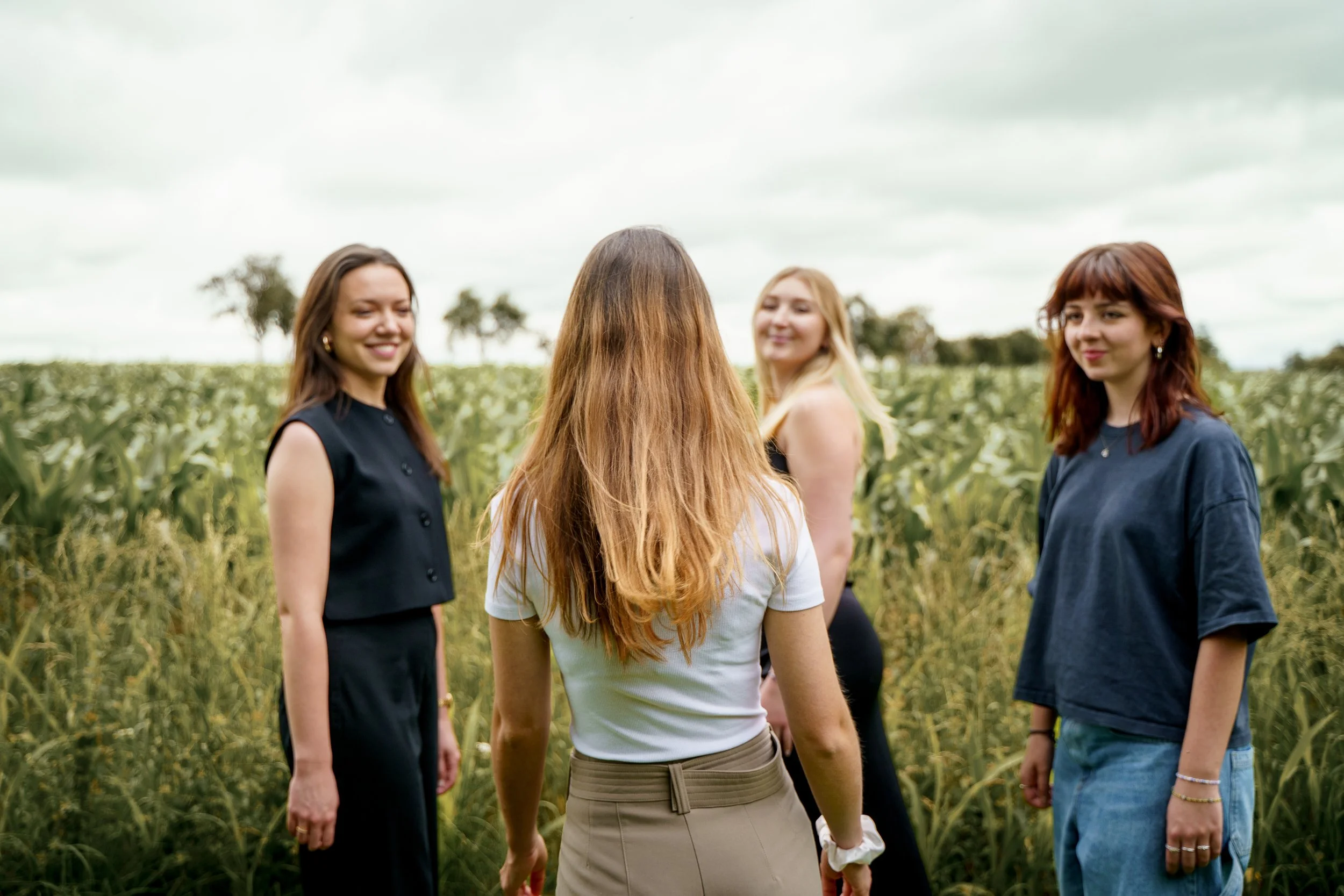 Vier Frauen stehen in einem Feld, lachen und unterhalten sich bei bewölktem Himmel.