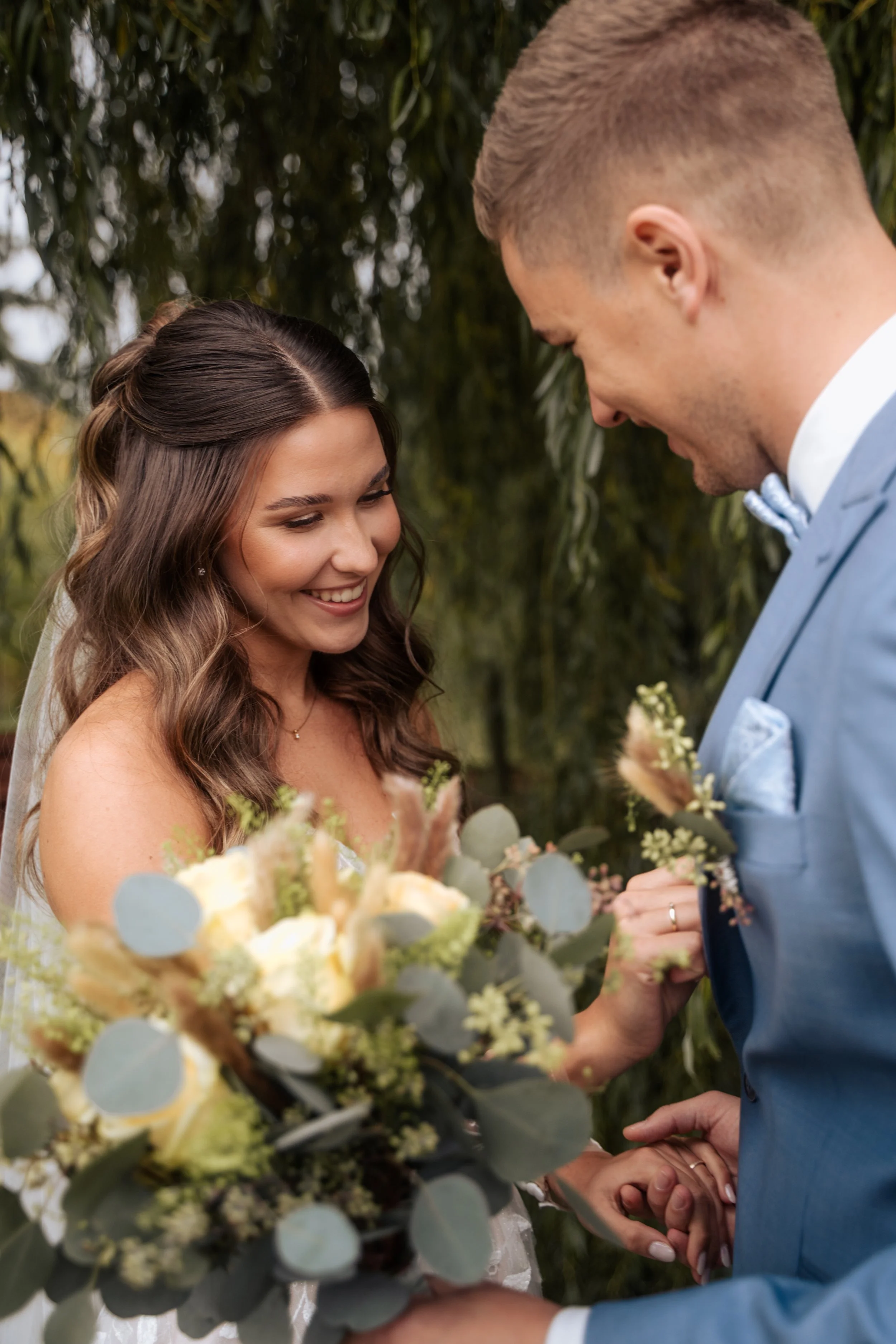 Ein Brautpaar bei einer Hochzeit, der Bräutigam hält die Hand der Braut, im Vordergrund ist ein Blumenstrauß zu sehen.