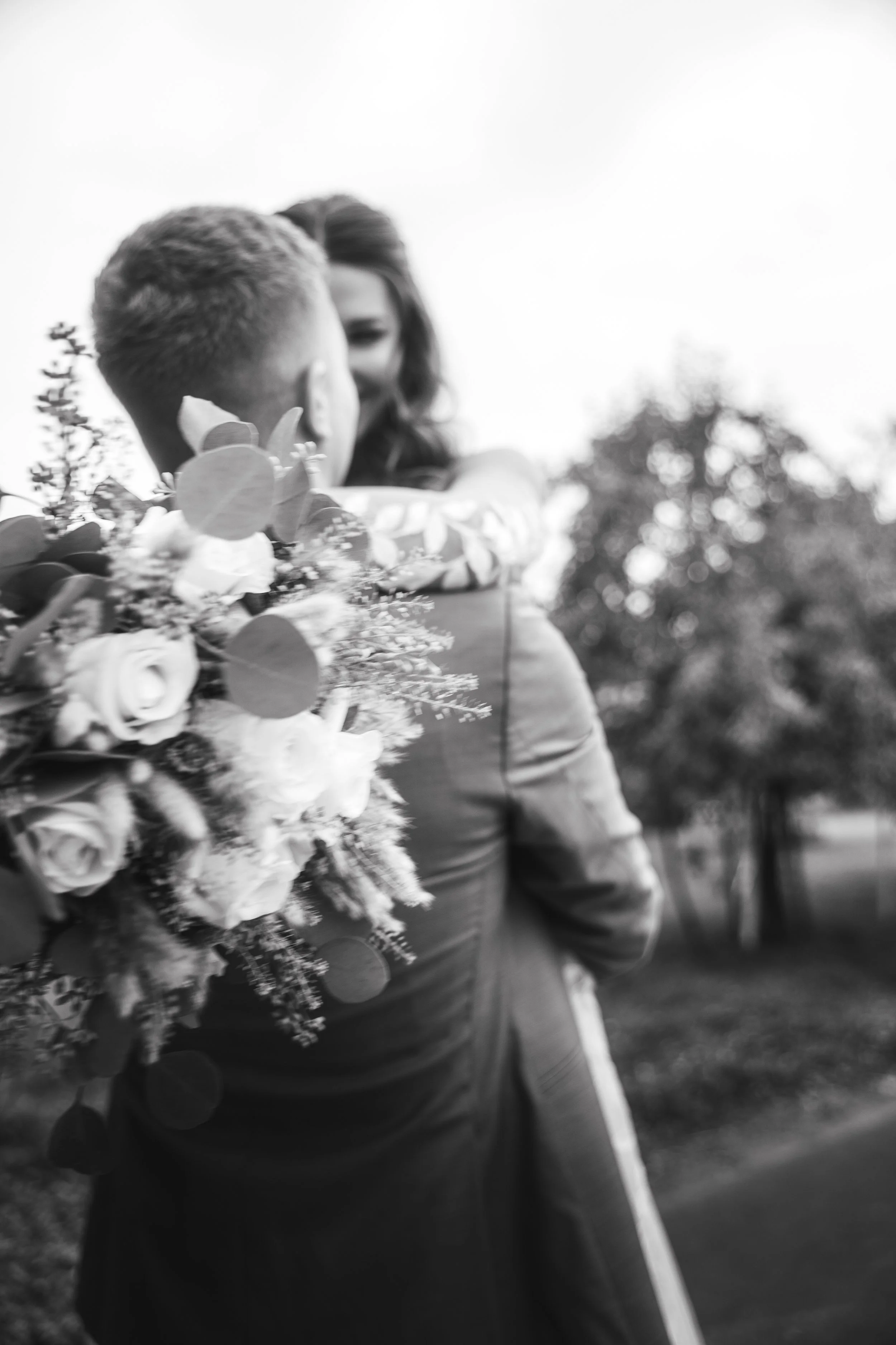 Zwei Personen, eine hält einen Blumenstrauß, draußen im Freien, unscharfer Hintergrund mit Bäumen, schwarz-weiß Foto