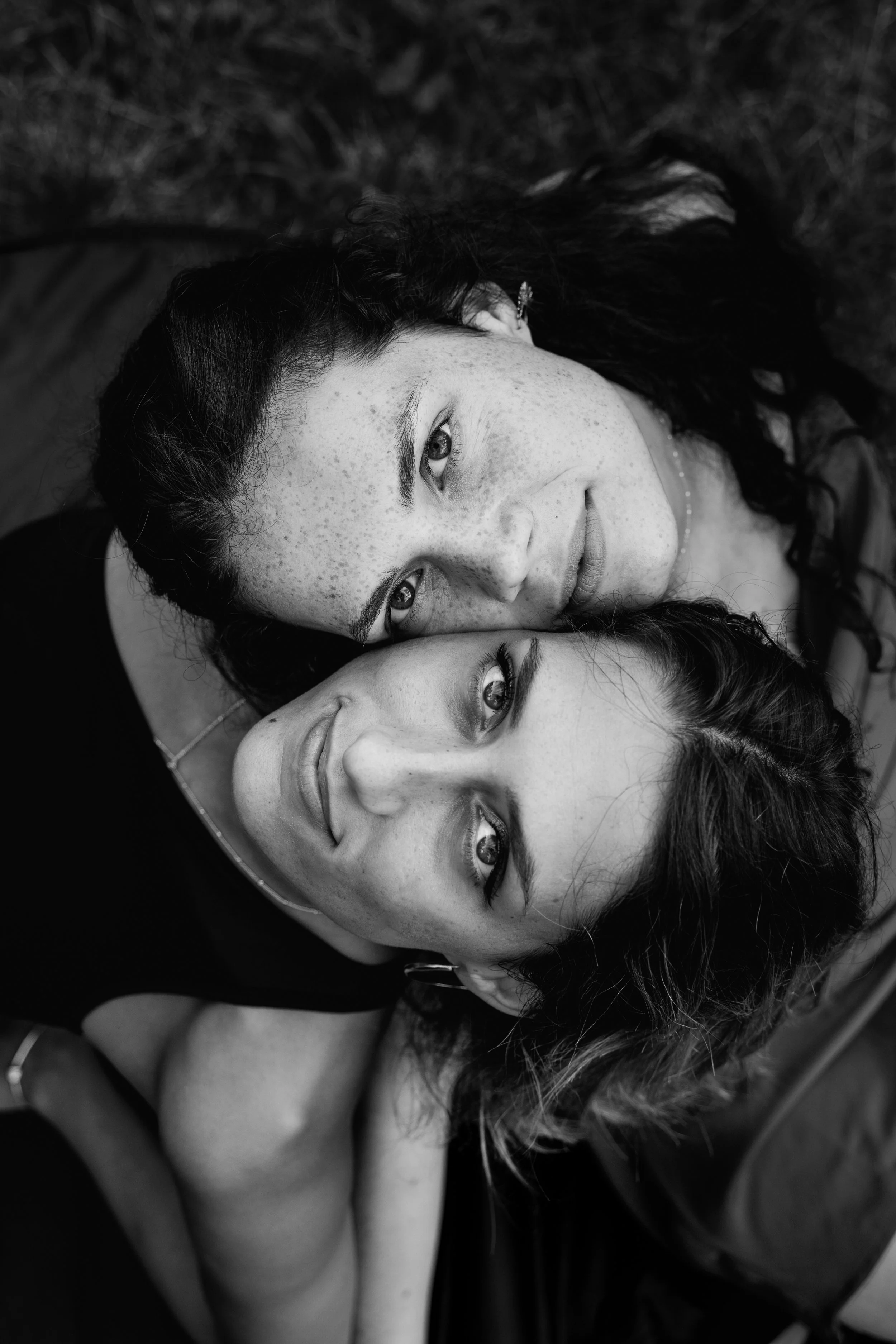 Zwei Frauen liegen nah beieinander, eine schaut direkt in die Kamera, die andere hat die Augen geschlossen.