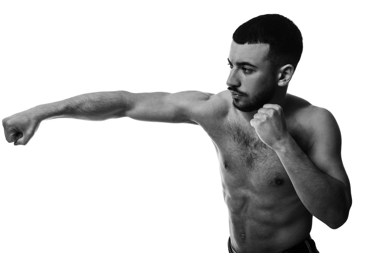 Männerlicher Kämpfer in einer Kampfsporthaltung, der nach vorne schlägt, mit einem nackten Oberkörper auf weißem Hintergrund.