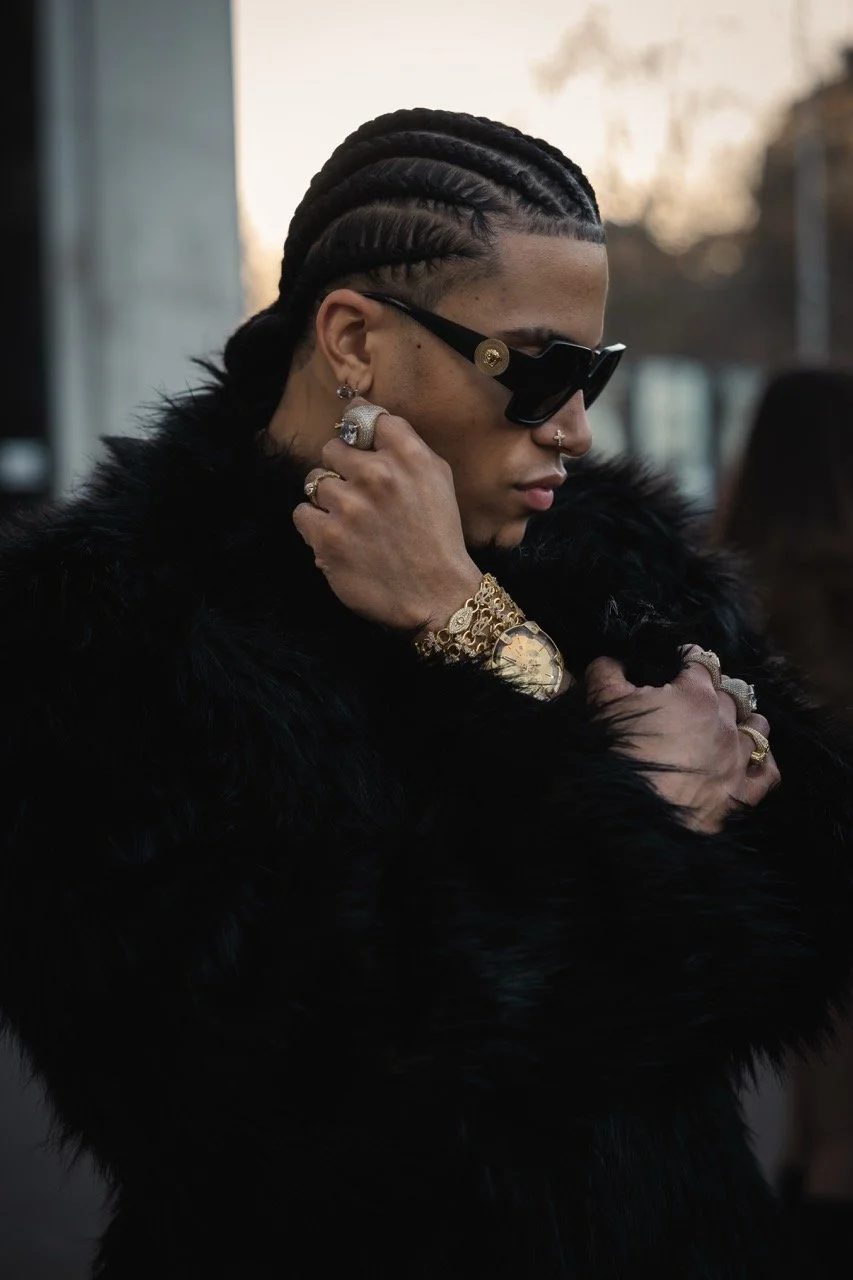 Modepersonen mit schwarzen Zöpfen, Sonnenbrille, Schmuck und Pelzmantel in urbaner Umgebung bei Sonnenuntergang.