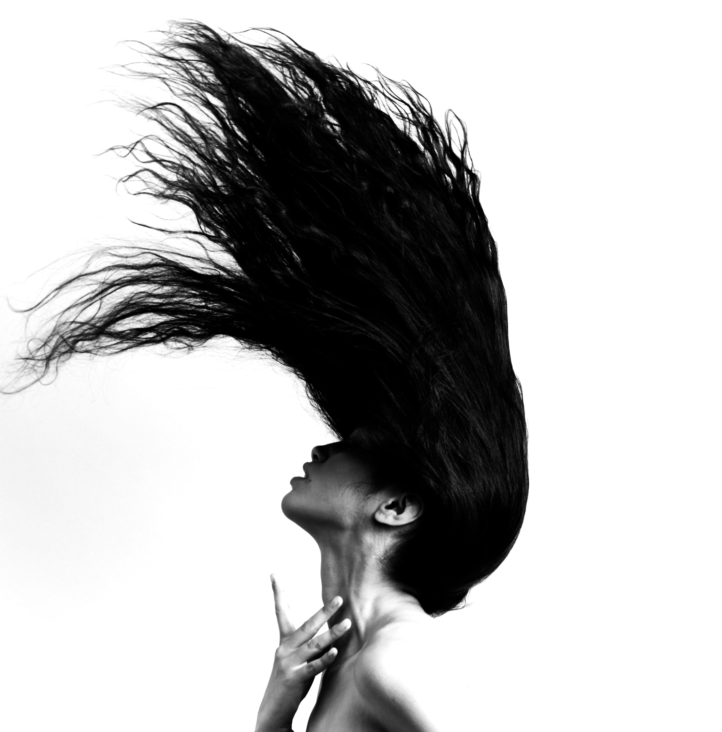 Black and white photo of a woman with long hair flowing in the air, her eyes closed, and her hand resting on her chest with fingers gently touching her collarbone.