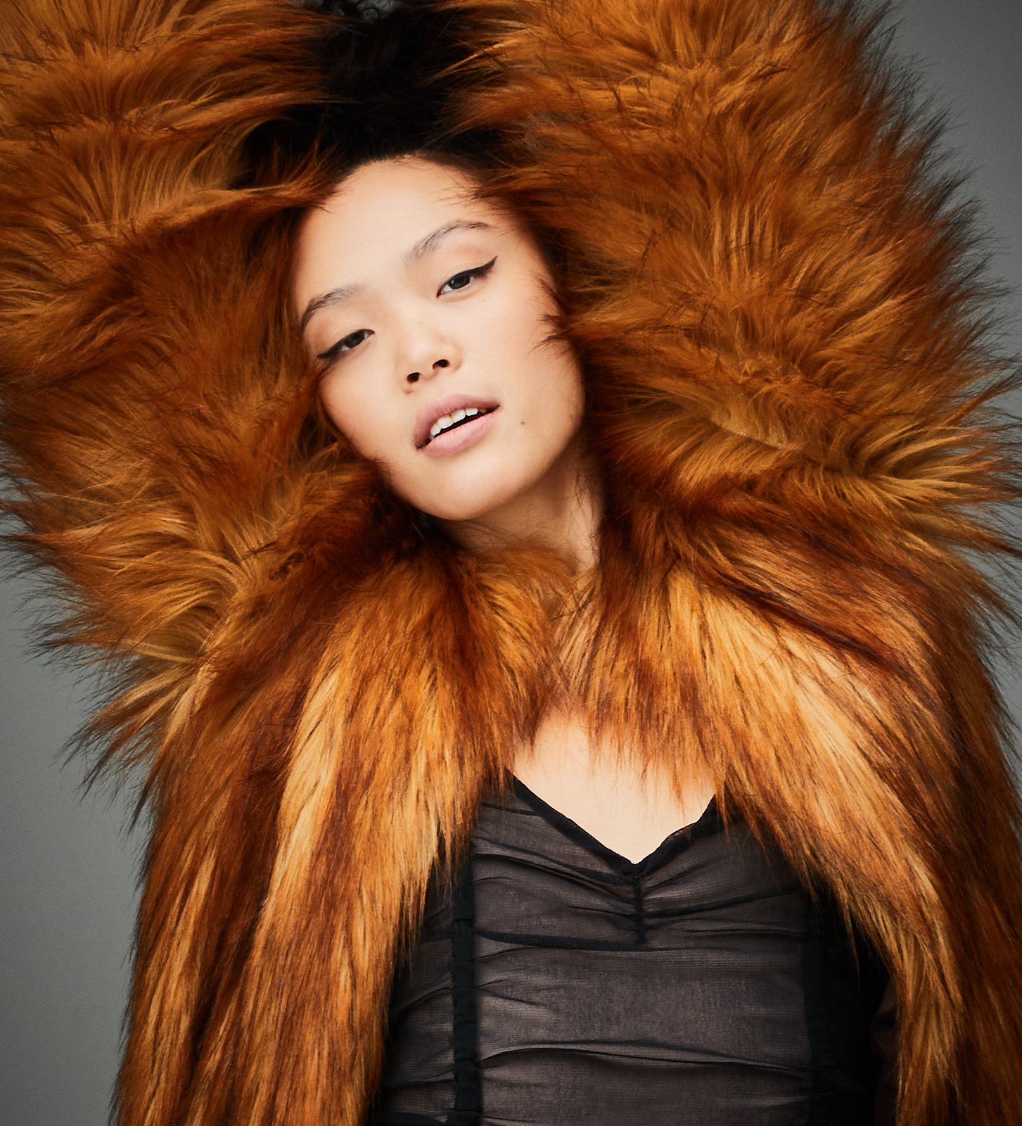 A woman with long, flowing hair wearing a large, fluffy orange fur coat with a black top underneath.