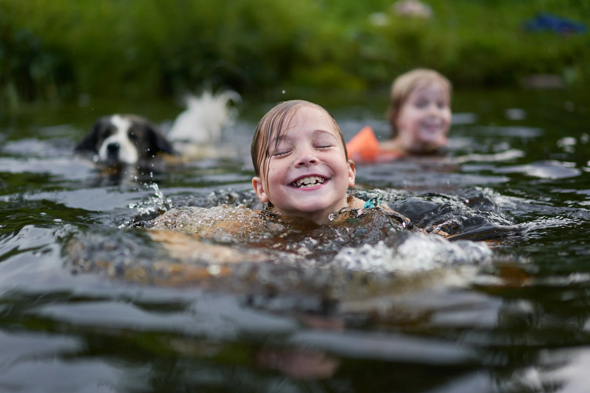 One girl and boy swimming in the river with their dog