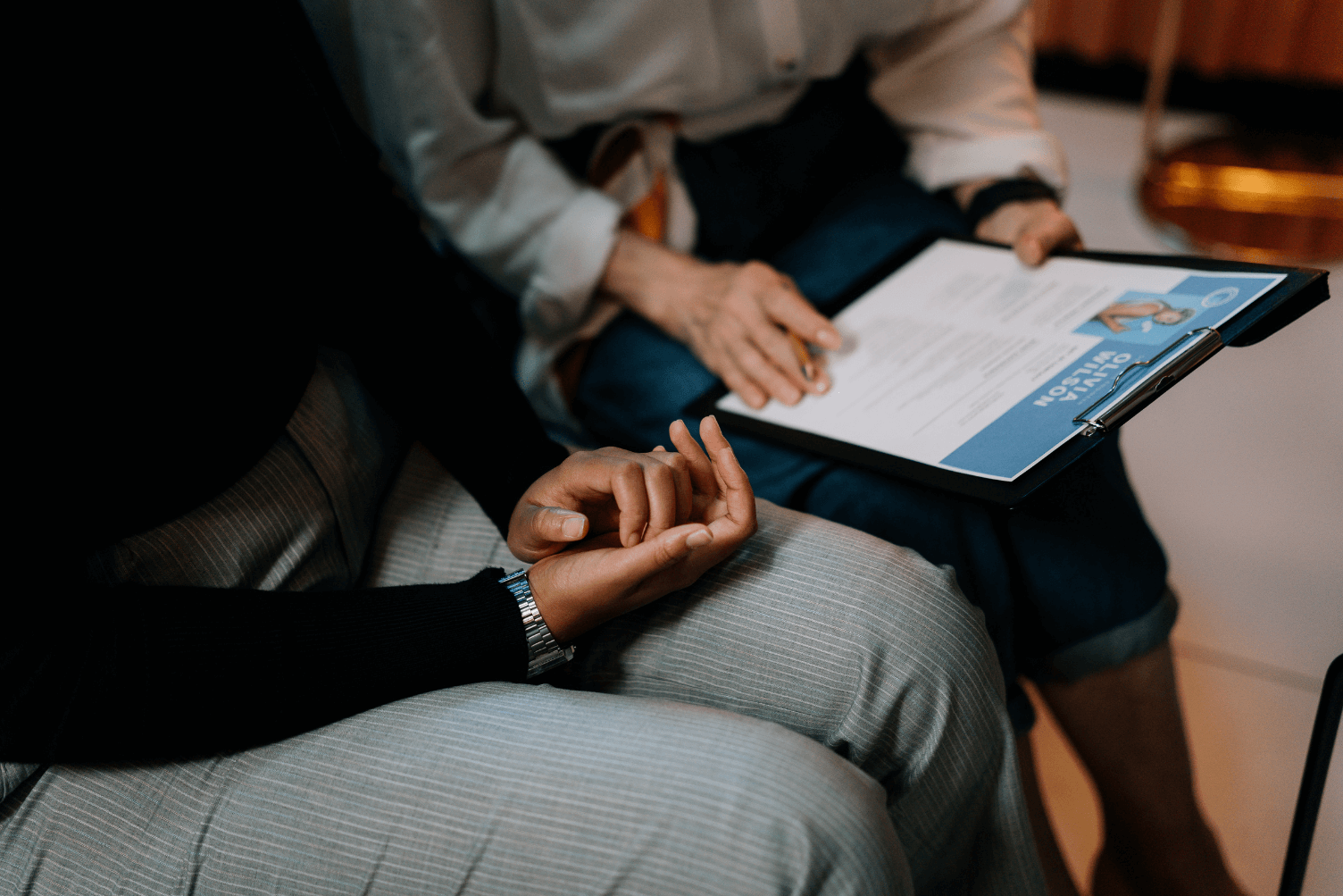 An executive woman sits beside another woman, holding a clipboard, discussing a cover letter formula.