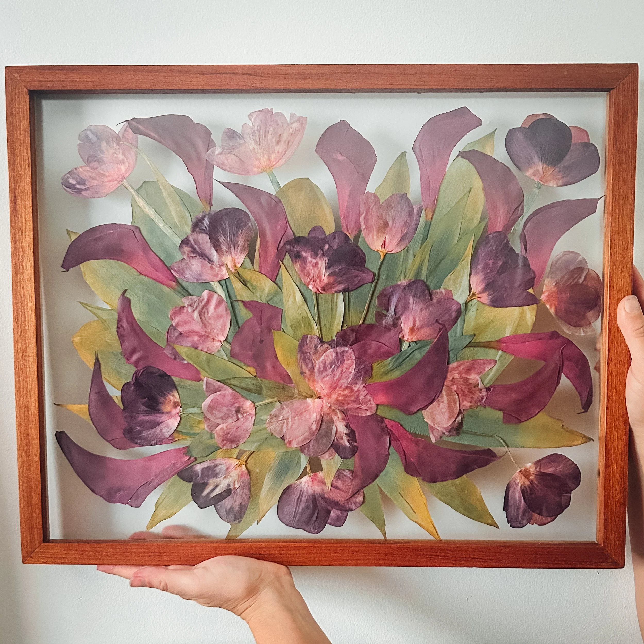 A person holding a framed botanical print of purple and green leaves against a white background.