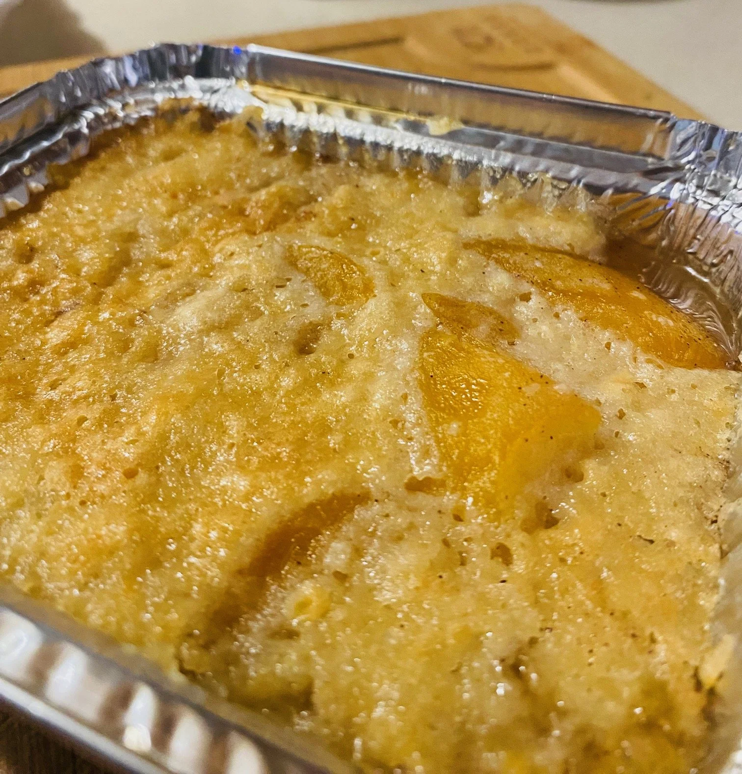 Close-up of a baked dish in a foil container with a golden, crispy top and some visible potato slices.