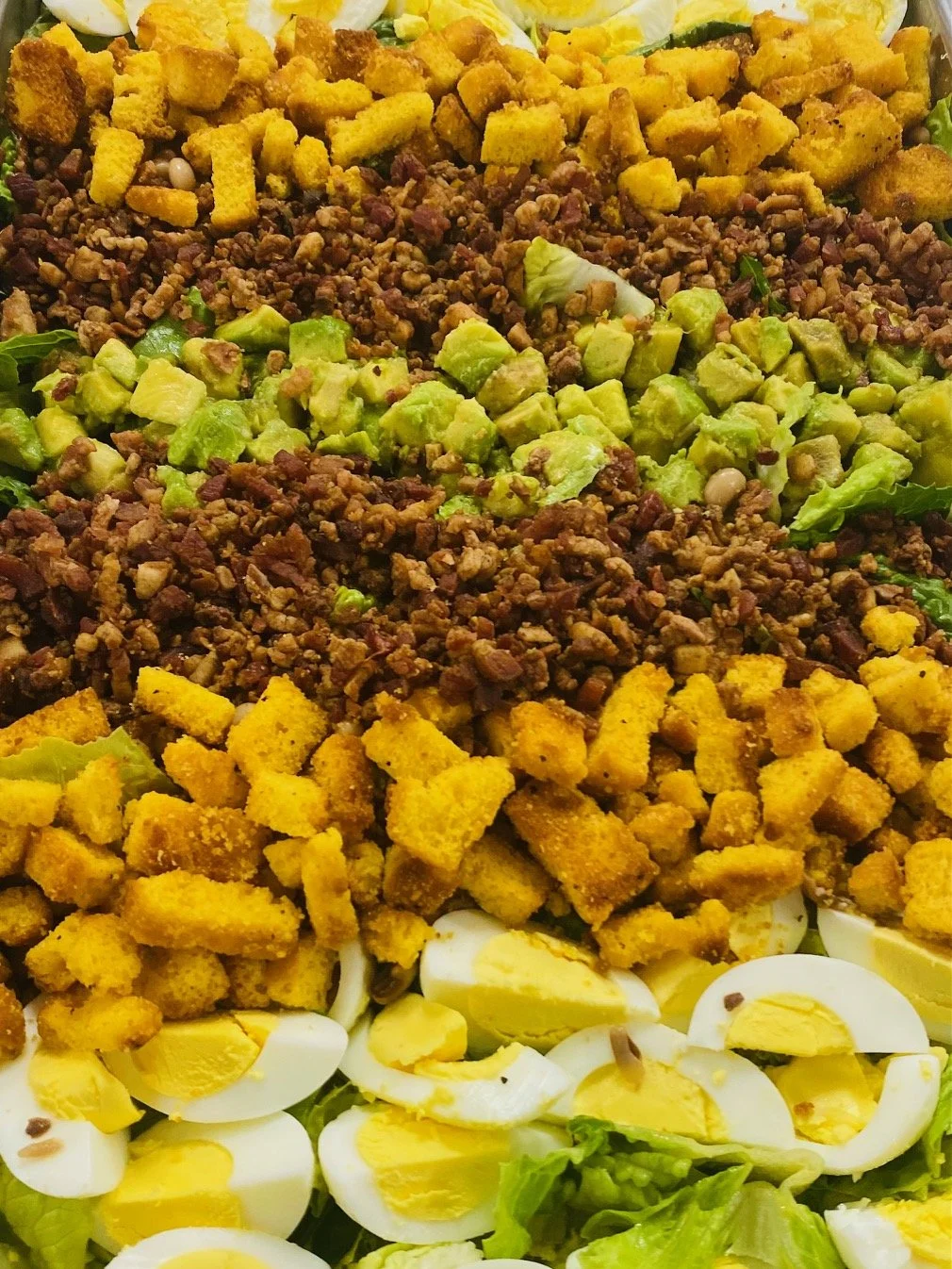 Assorted salad with chopped hard-boiled eggs, crumbled cooked ground beef, crispy fried chicken pieces, and diced avocado on mixed greens.