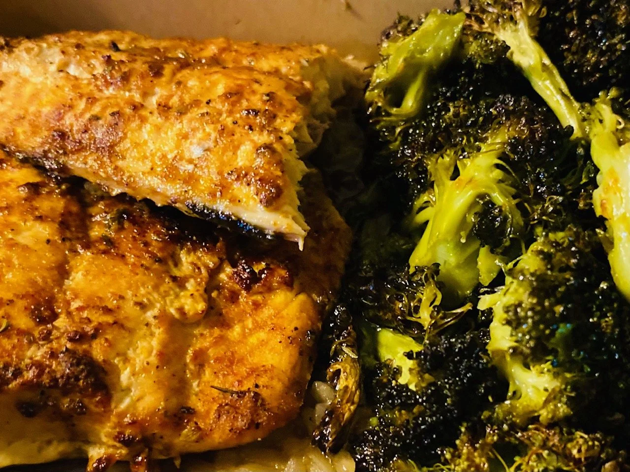 Close-up of cooked chicken breast with a golden-brown crust and grilled broccoli florets.