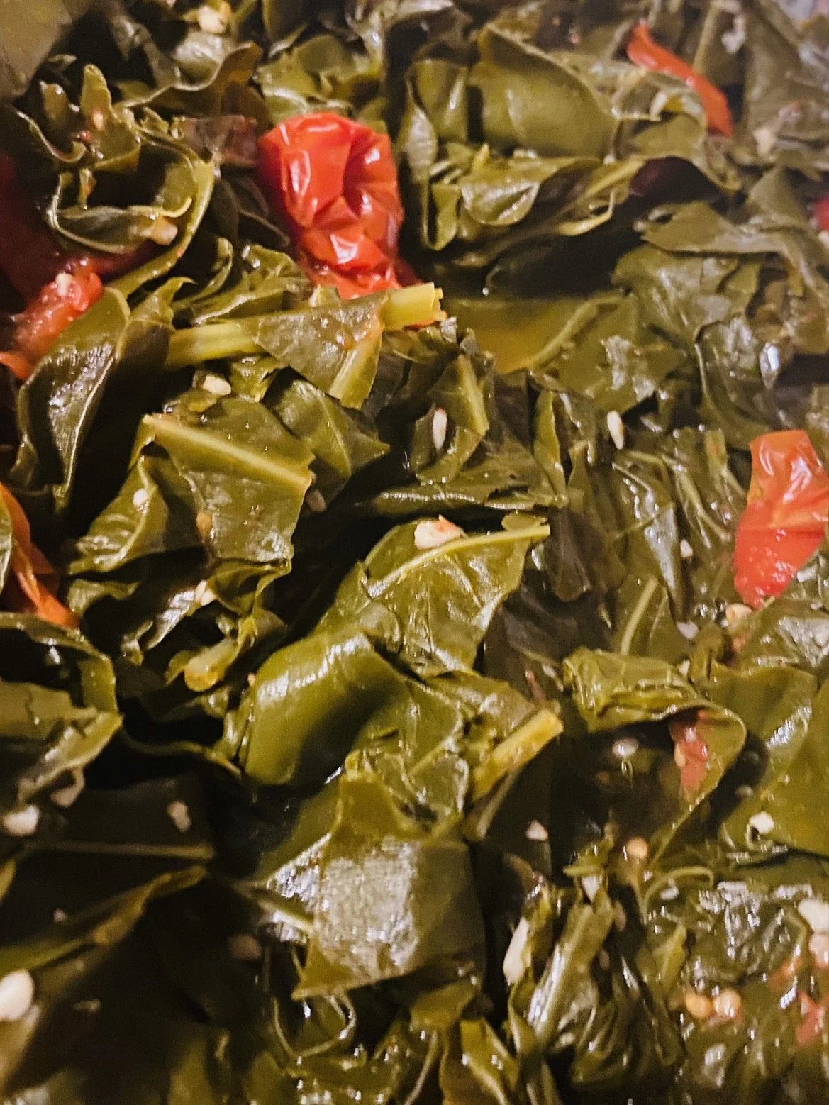Close-up of cooked collard greens with chopped garlic and small pieces of red pepper.