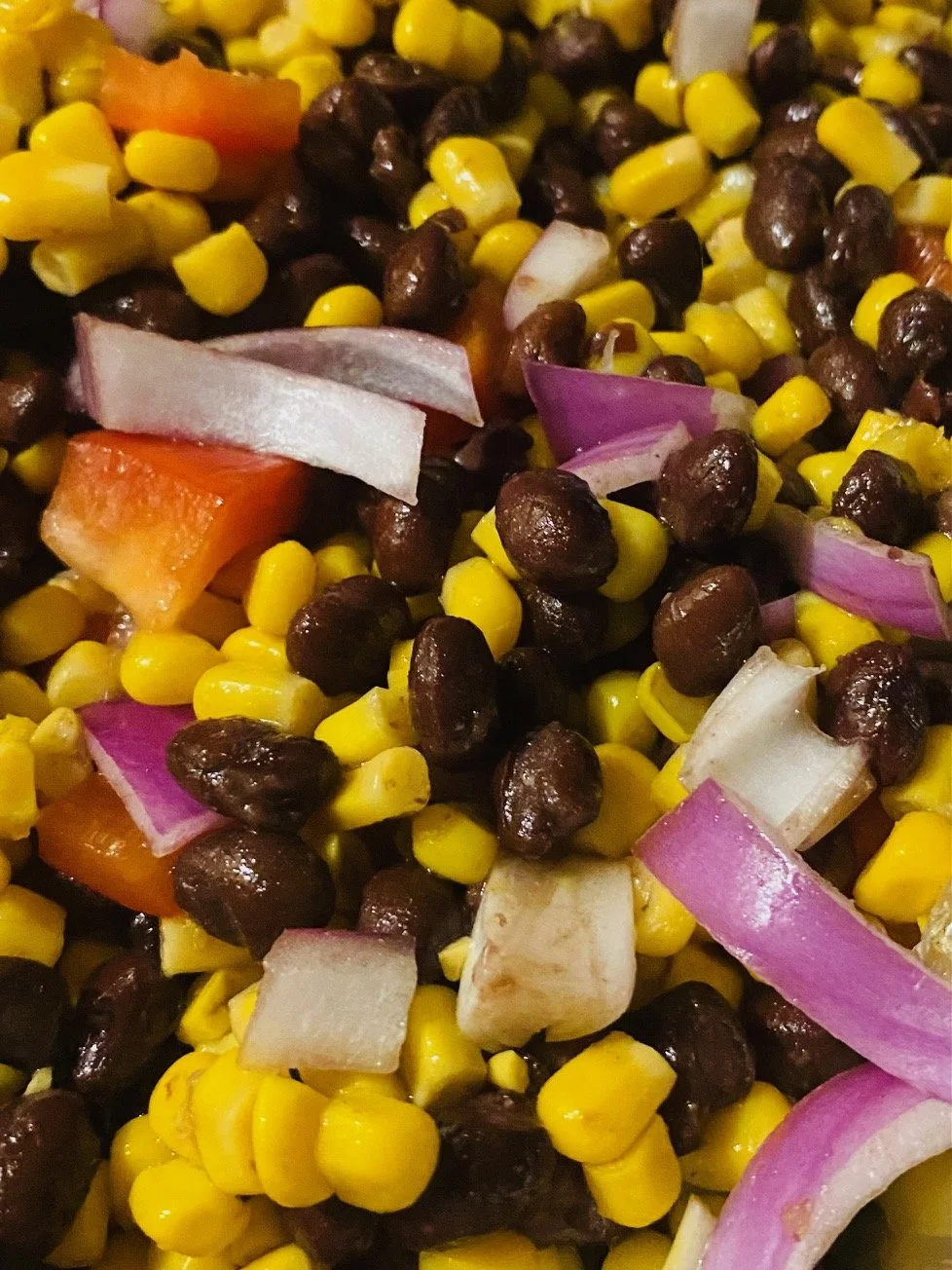 Close-up of a mixed corn and bean salad with chopped red onions and tomatoes.