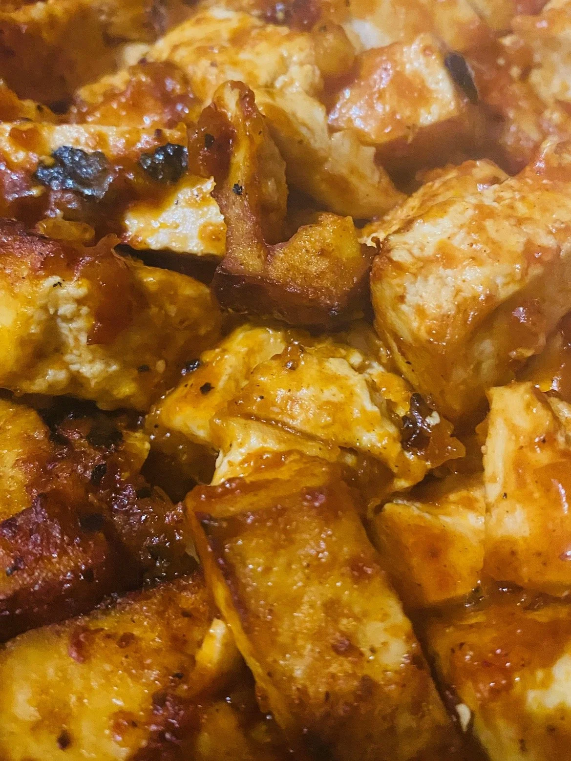 Close-up of cooked chicken pieces with a reddish sauce.