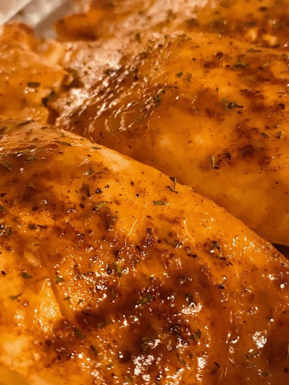 Close-up of seasoned, cooked chicken breasts with visible herbs and spices, possibly grilled or baked.