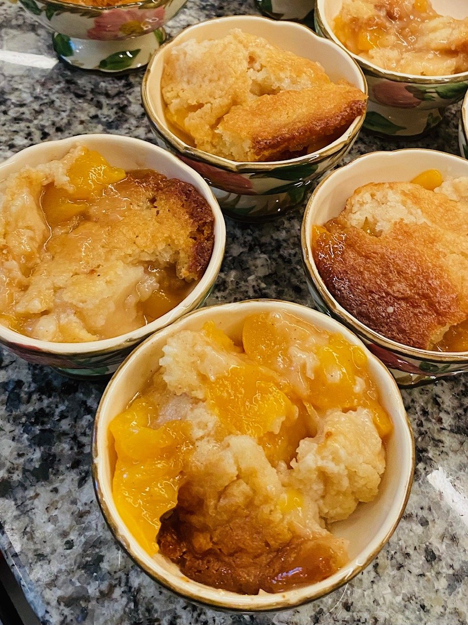 Baked peach cobbler in decorative bowls on a granite countertop.