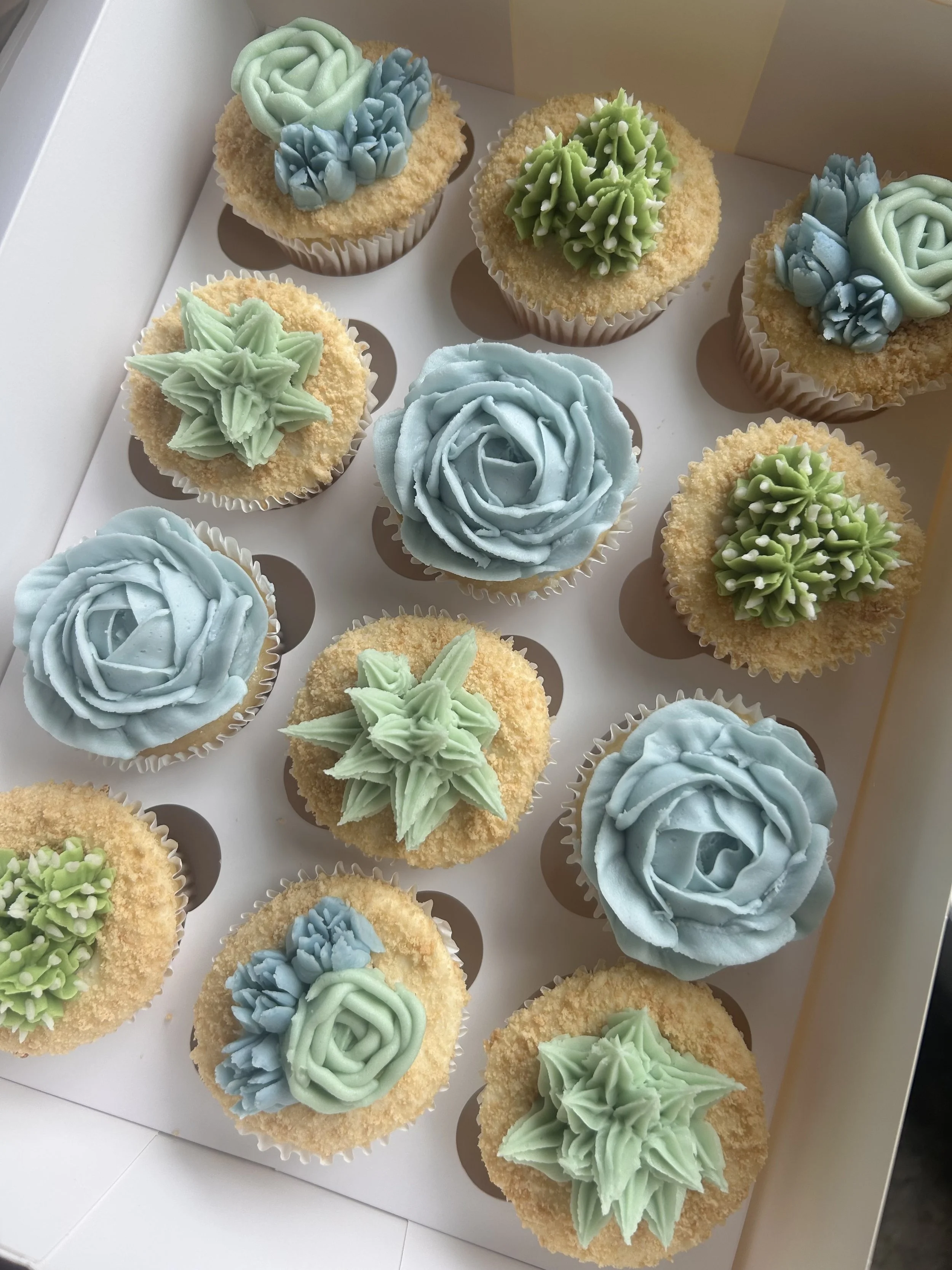 Cupcakes decorated as succulents with green and red icing, arranged in a box.