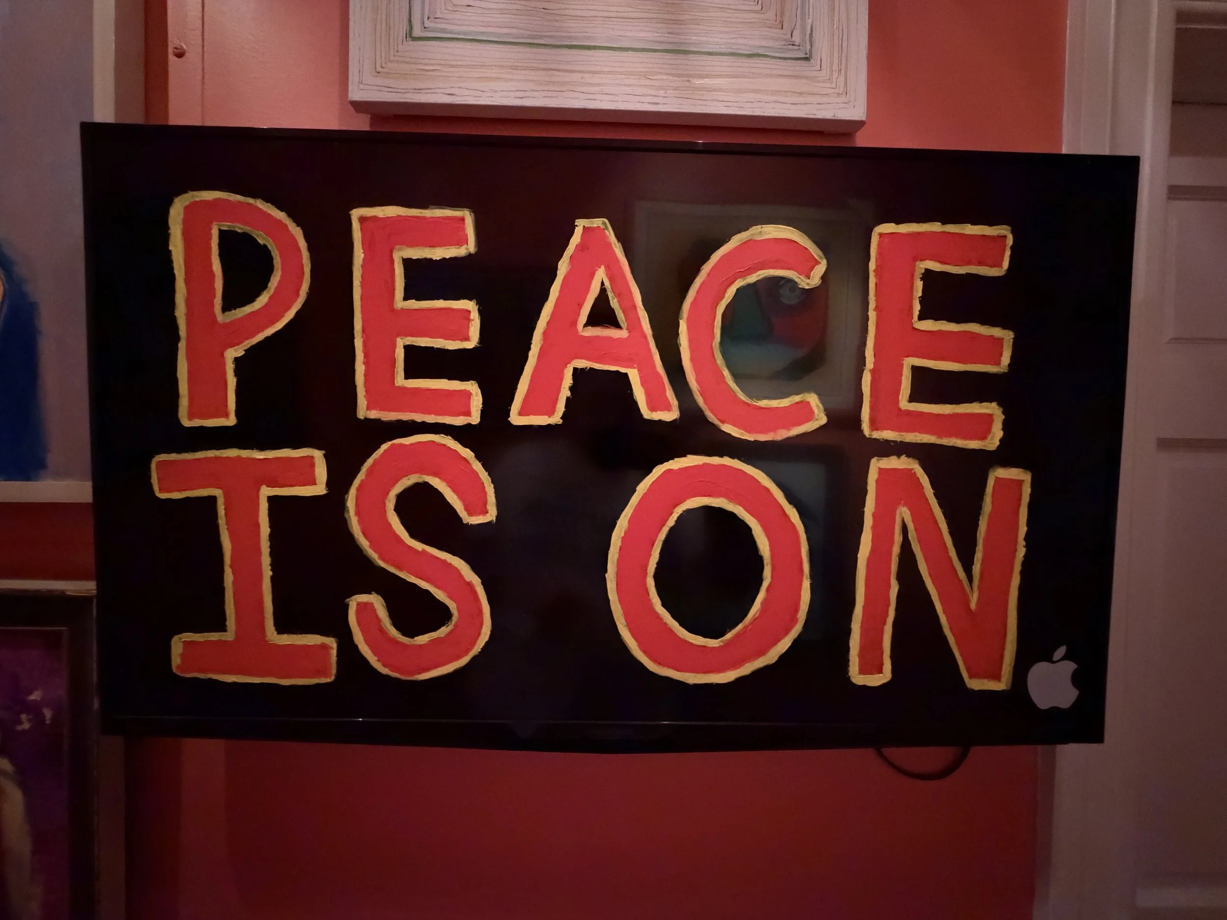 A black poster with large red and yellow letters spelling 'PEACE' partially visible, placed on a red wall.